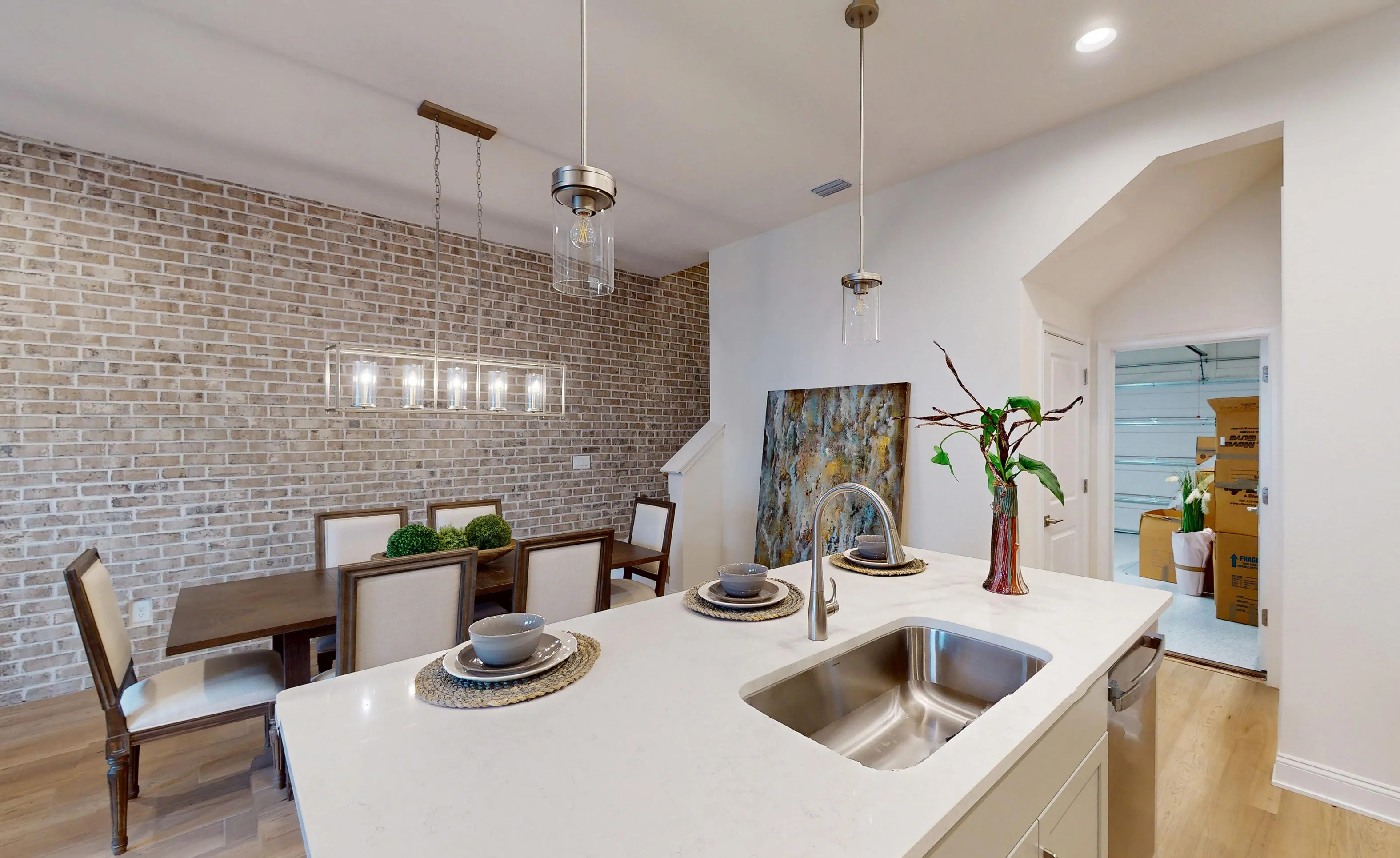 Kitchen with a white quartz island, stainless steel sink, and adjacent dining area featuring a tan brick accent wall.