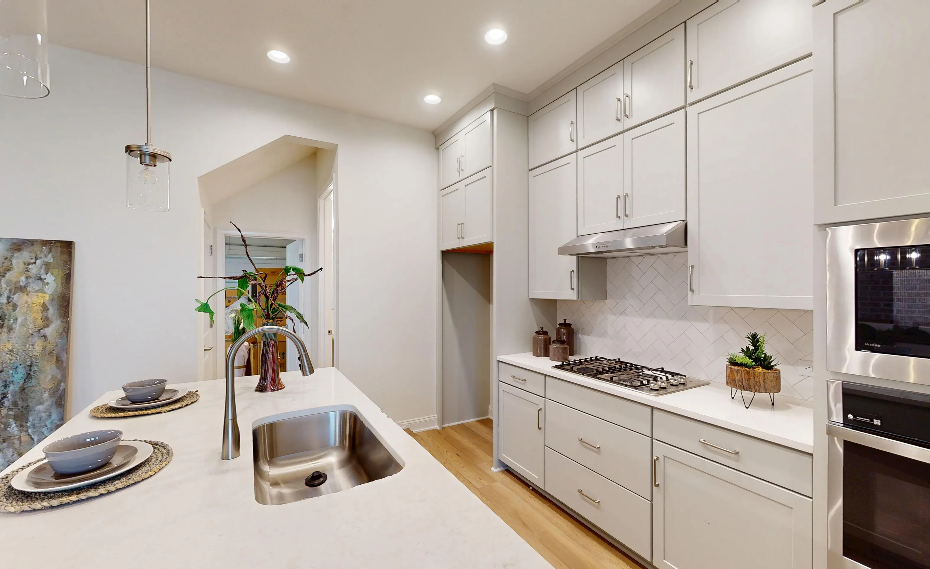 Kitchen with white cabinets, quartz countertops, a central island with a sink, and a herringbone-tiled backsplash.