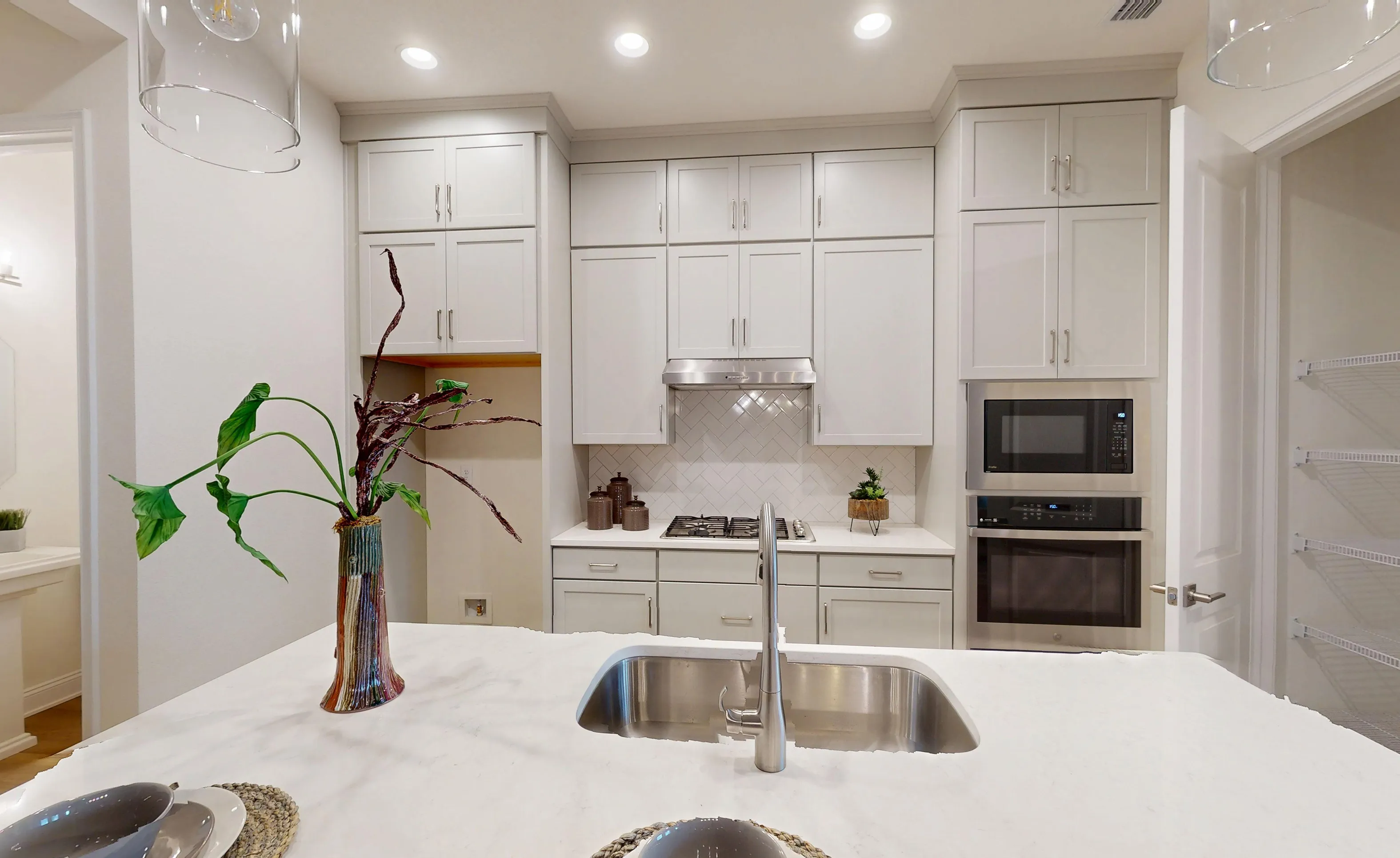 Kitchen in the Castillo home featuring light gray cabinets, a white herringbone backsplash, and a large center island.