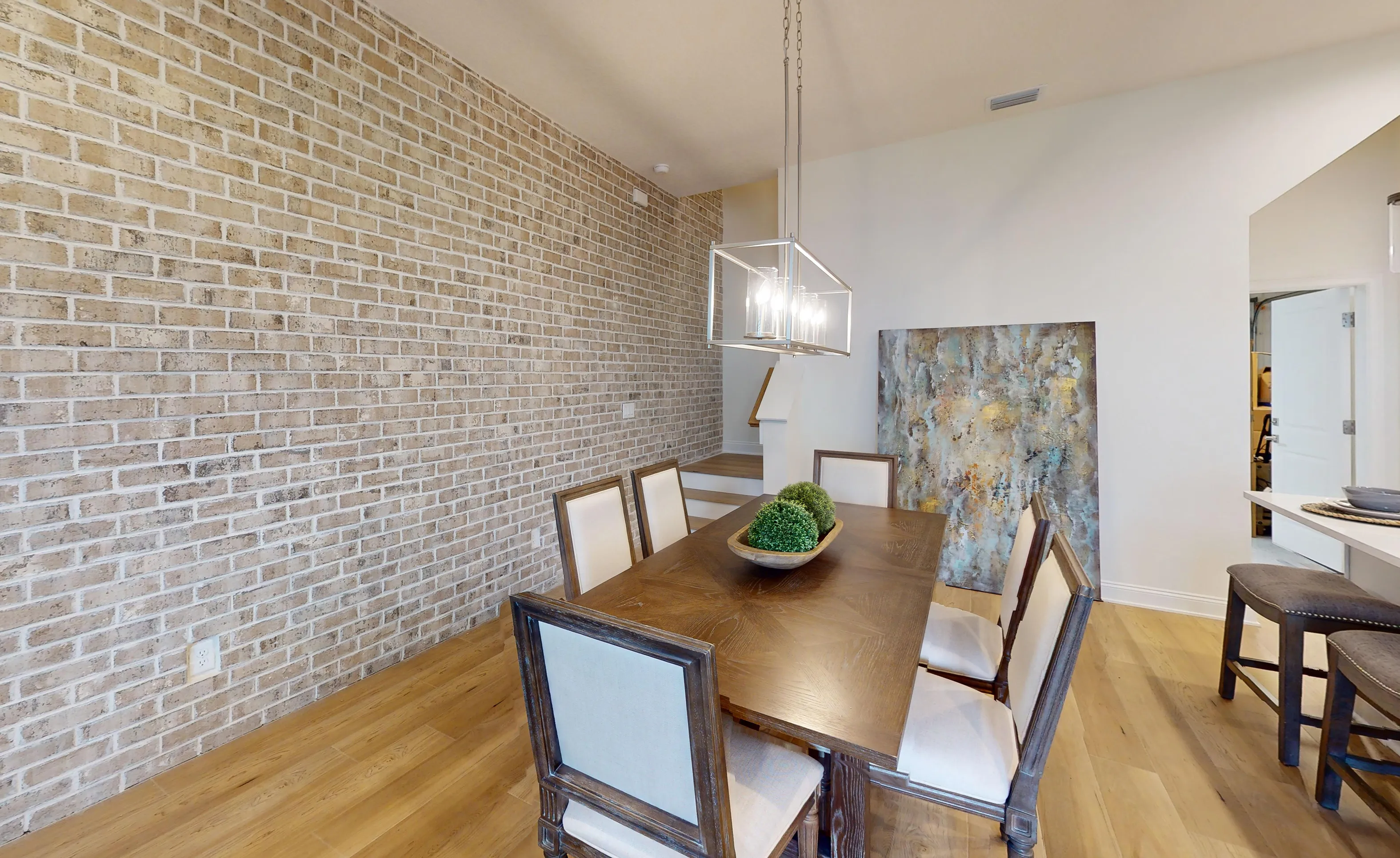 Dining room with wood table, upholstered chairs, a brick accent wall, and a rectangular pendant light fixture.