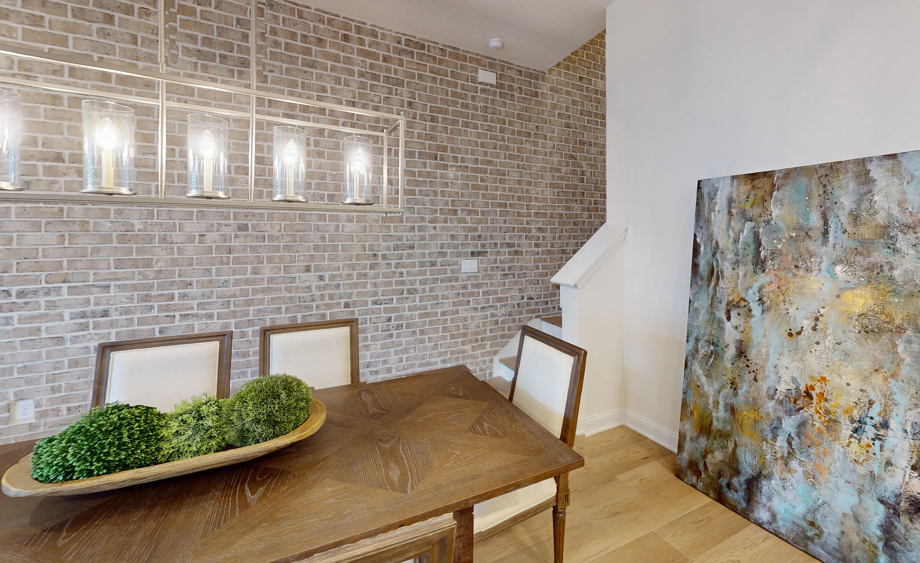 Dining room in the Castillo plan featuring a brick accent wall, rectangular chandelier, and a wood dining table.