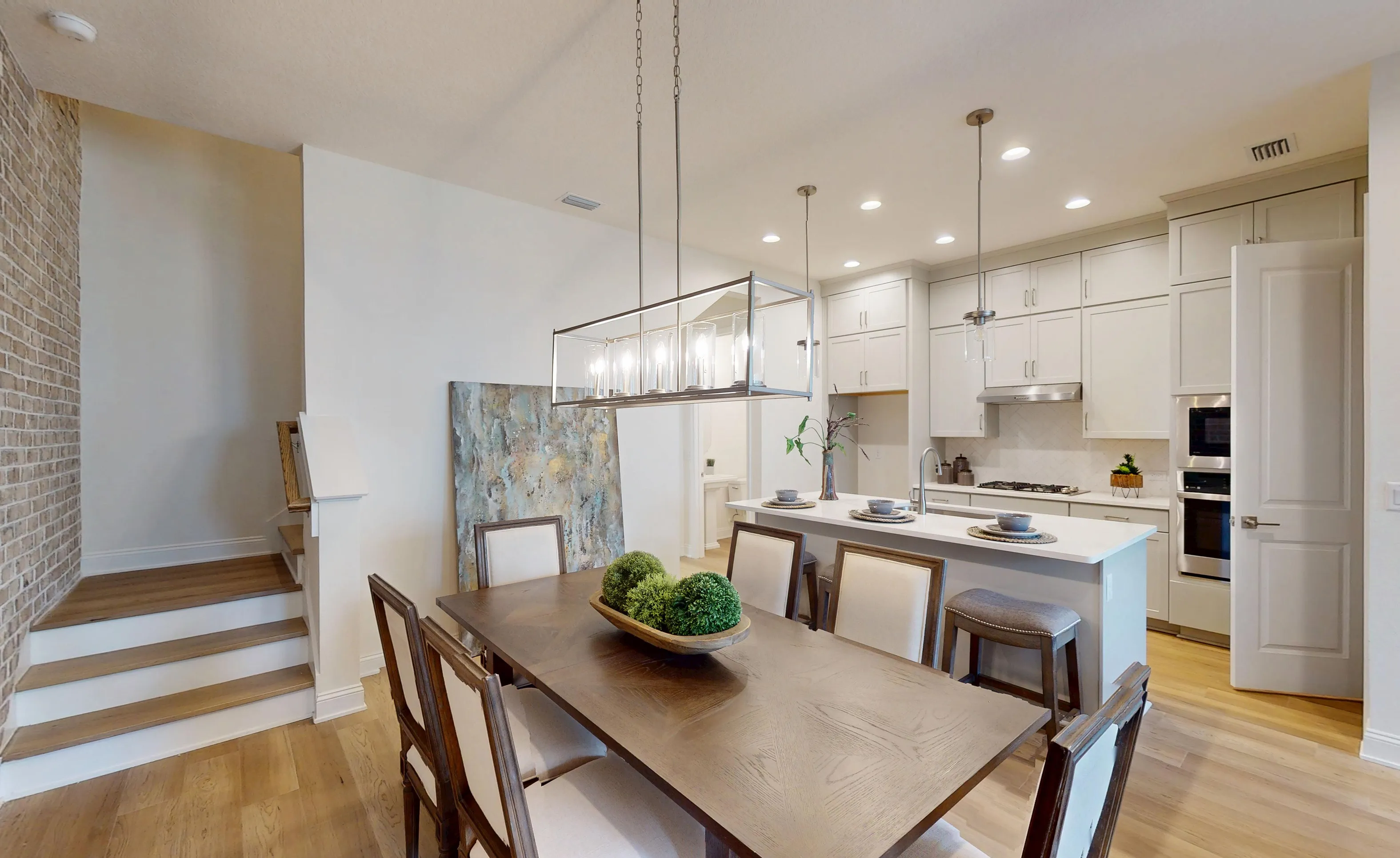 Dining room in the Castillo plan featuring a wooden table, pendant lighting, and stairs adjacent to an open kitchen.