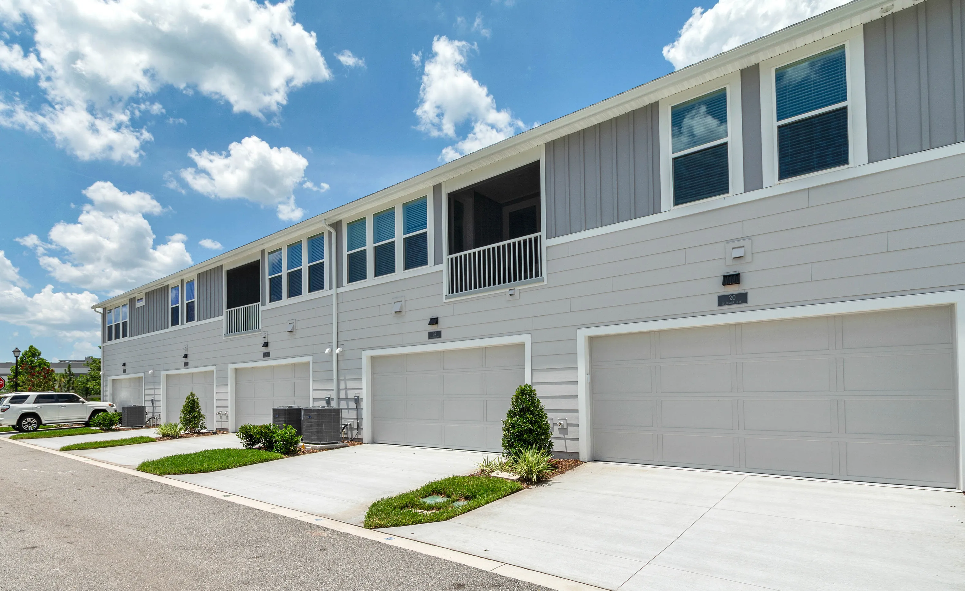 Rear exterior view of gray multi-family townhomes in Nocatee featuring concrete driveways and attached garages.