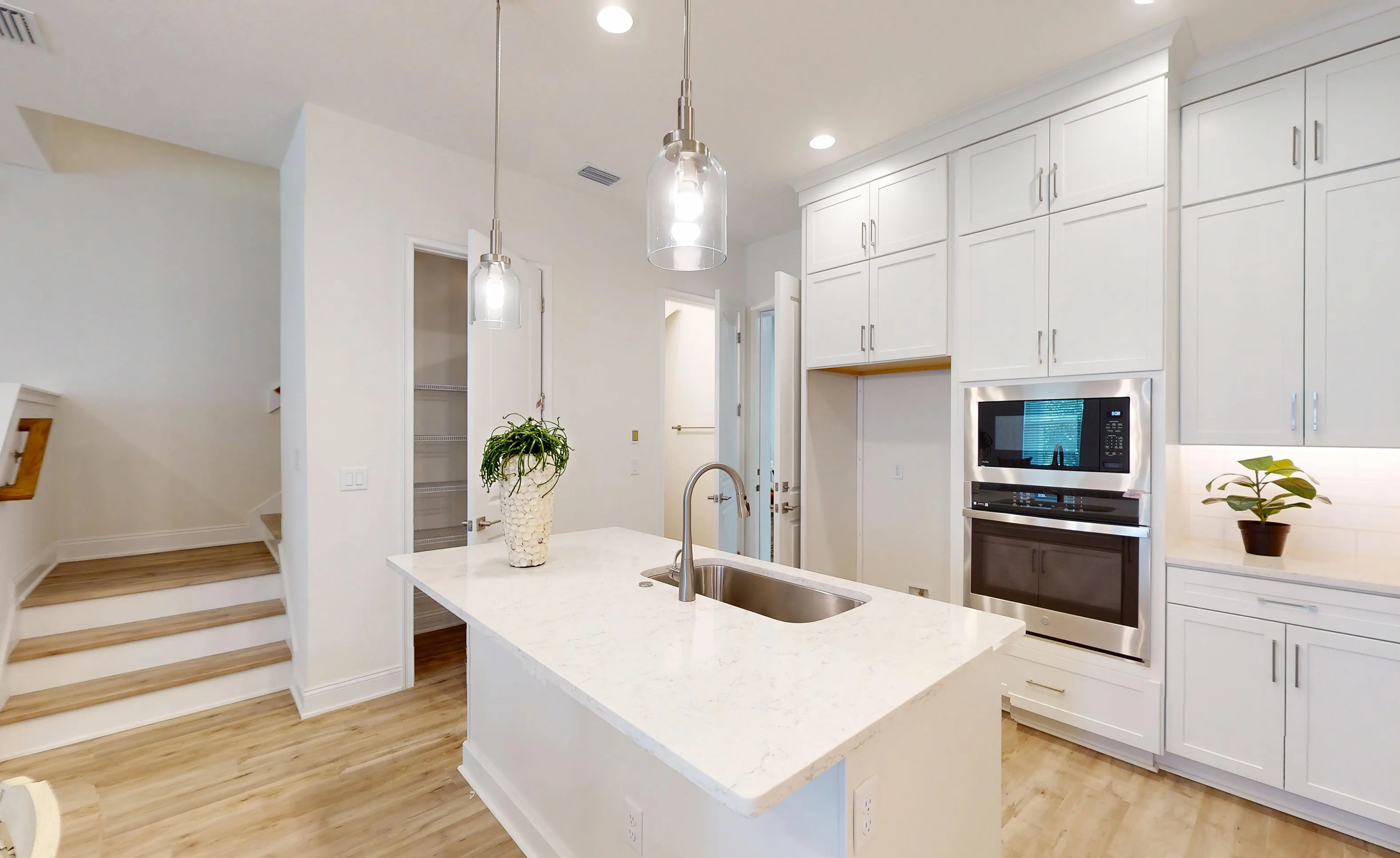 Kitchen of the Deleon plan with white cabinets, a central island with a sink, stainless steel wall oven, and wood flooring.