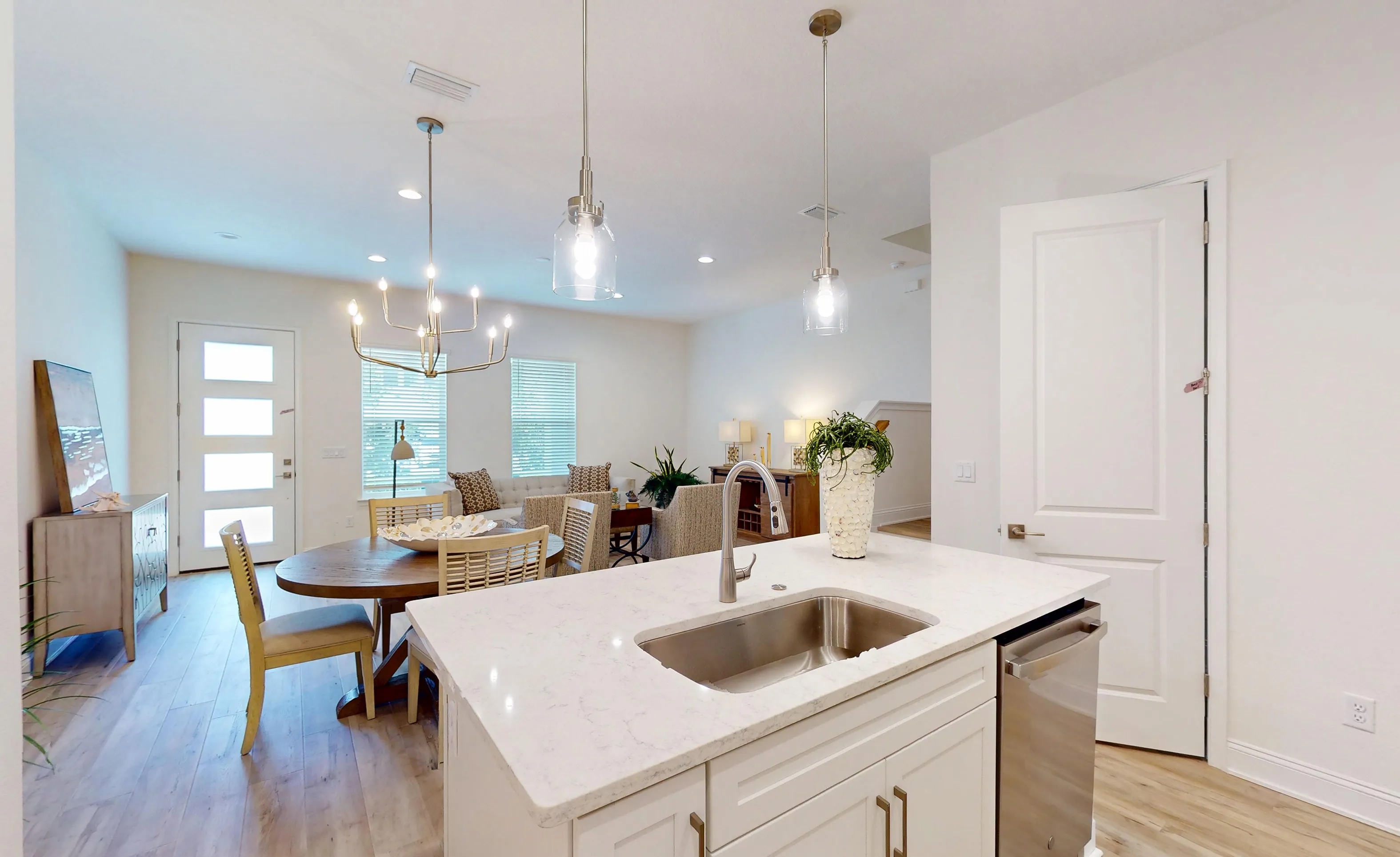 Kitchen island with a sink and white cabinets, overlooking a dining area with a wood table and chairs in the Deleon plan.