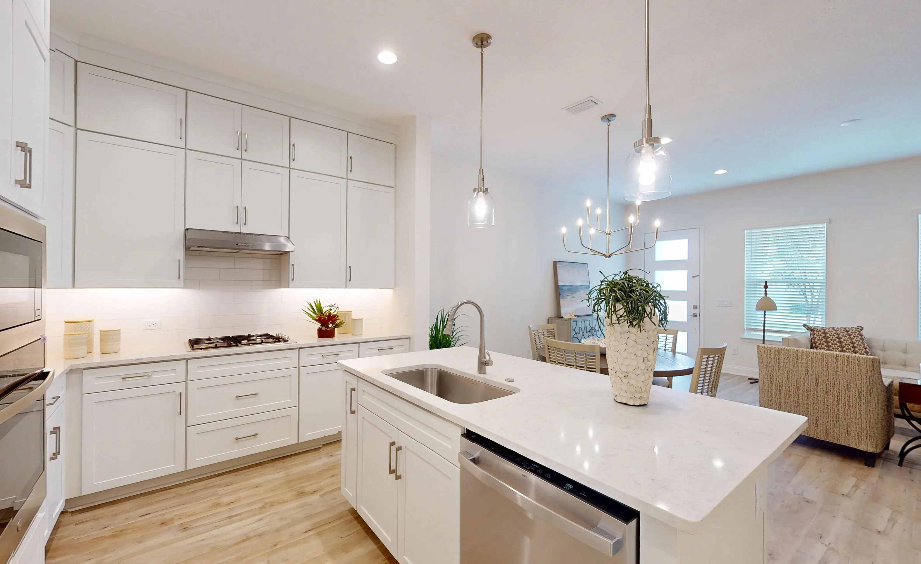 Kitchen in the Deleon floor plan featuring white cabinets, a central island with a sink, and an open view to the dining area.