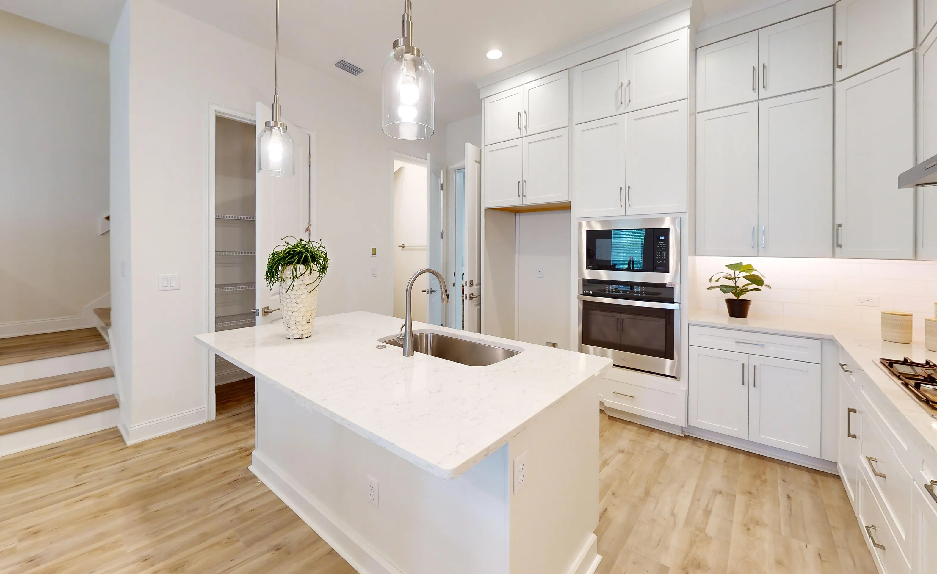 Kitchen of the Deleon plan featuring white cabinets, a central island with a sink, stainless appliances, and wood flooring.