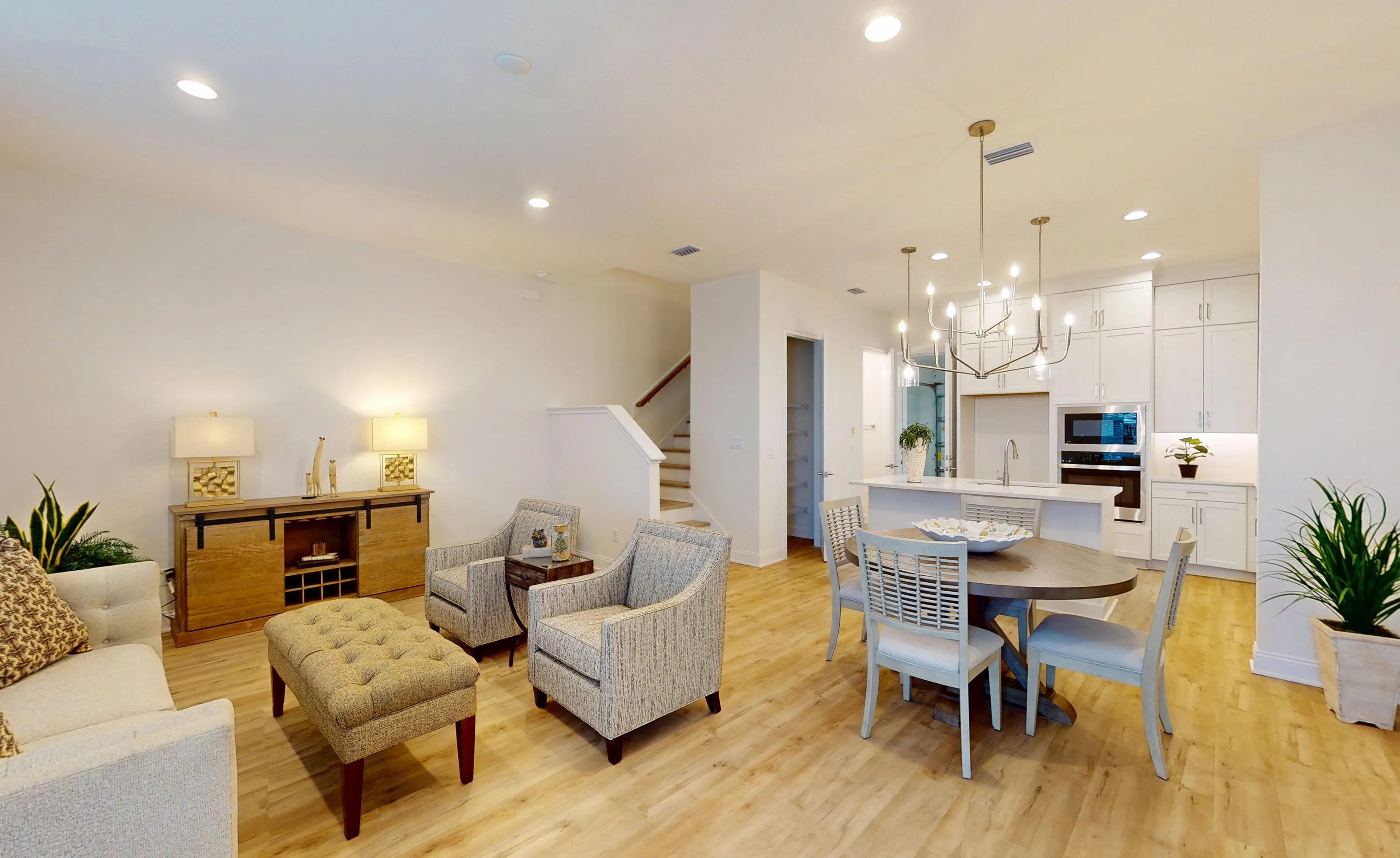 Open-concept living room and kitchen in the Deleon plan featuring light wood floors, a dining area, and white cabinetry.