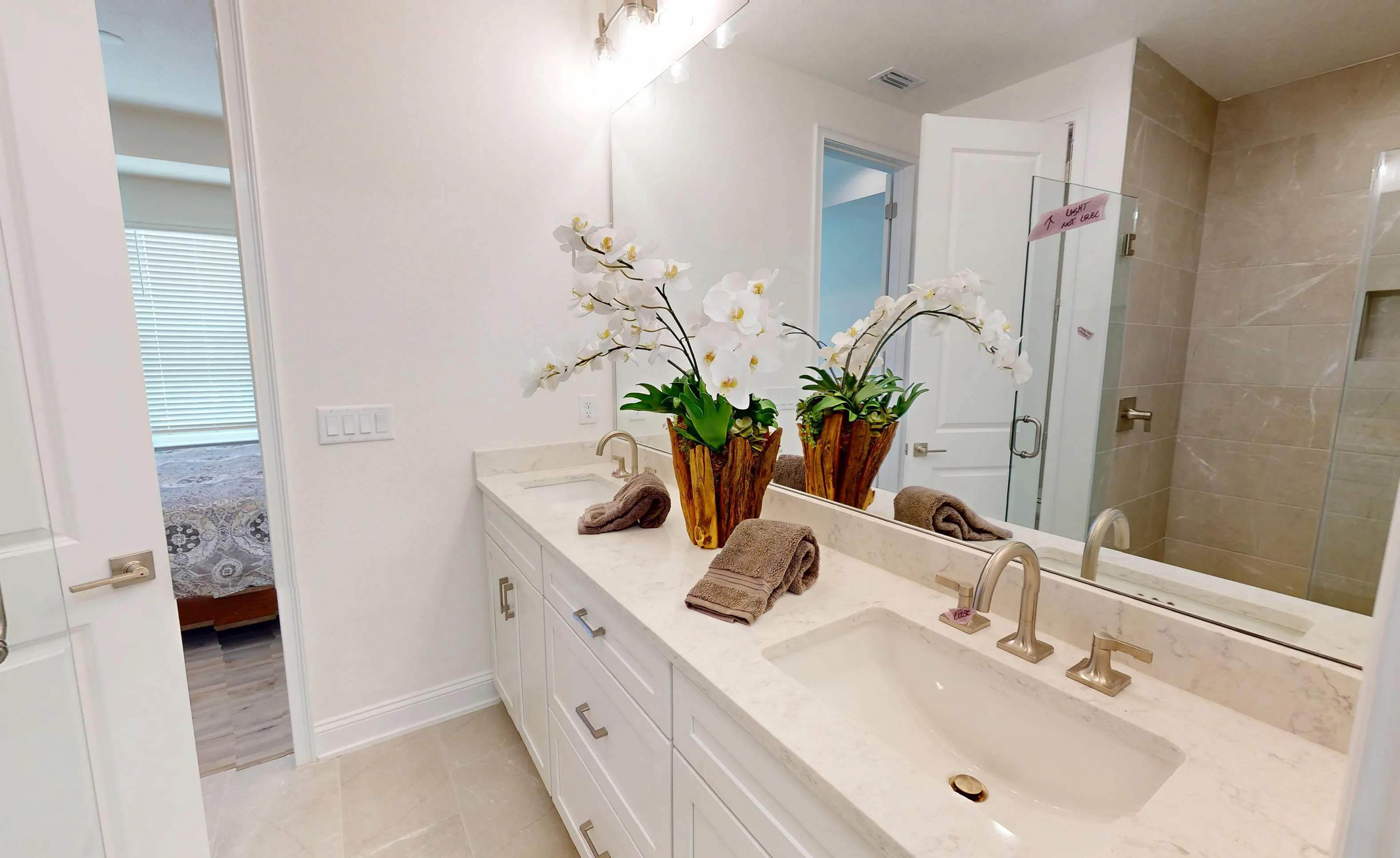 Secondary bath featuring a double vanity with white cabinetry, light stone countertop, and a tiled walk-in shower.
