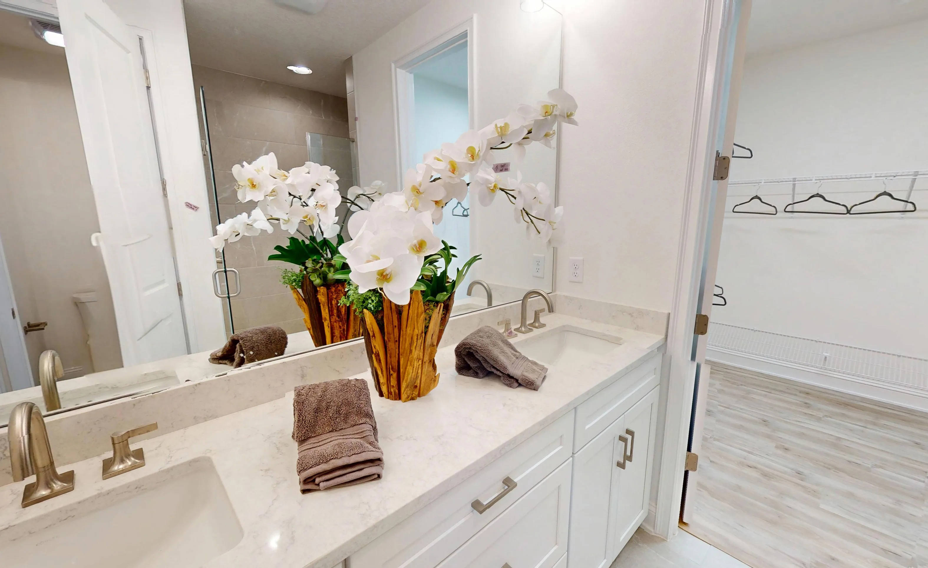 Primary bathroom vanity with light stone countertop, double sinks, white cabinets, and a doorway leading to a walk-in closet.
