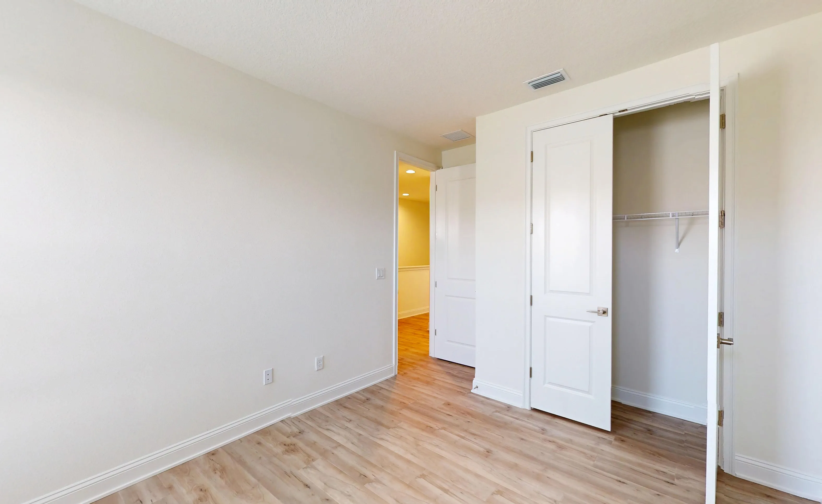 Secondary bedroom in the Deleon plan with light wood-look flooring, white walls, a walk-in closet, and an open doorway.