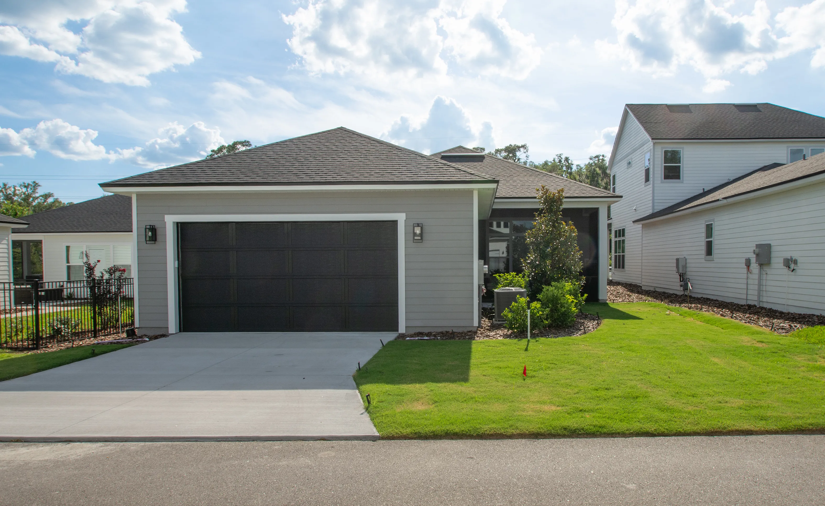 Side exterior of a Kona home in Oakmont featuring a grey-sided garage with a dark door, concrete driveway, and lawn.