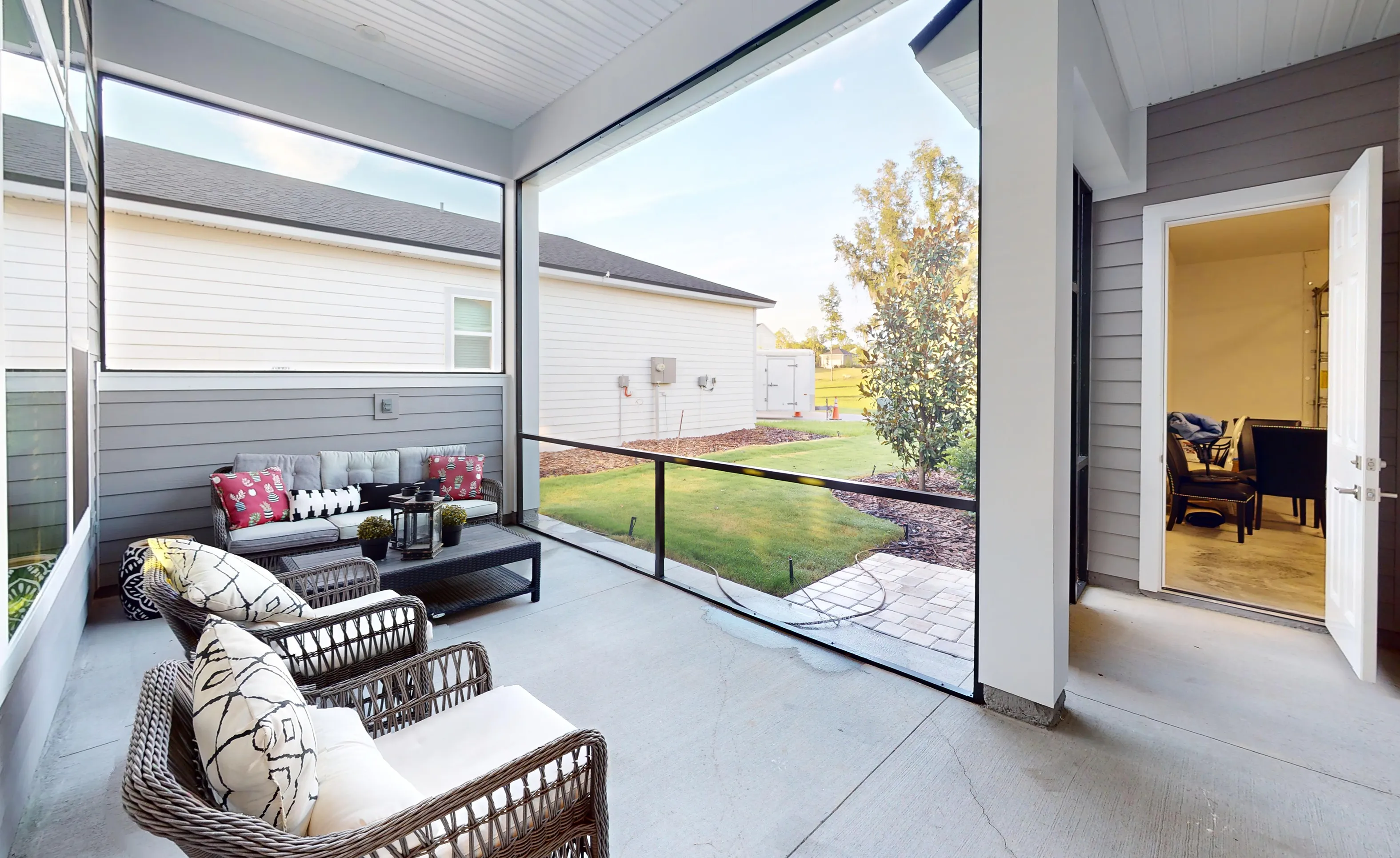 Screened lanai of the Kona plan featuring gray wicker seating, concrete flooring, and a view of a backyard.