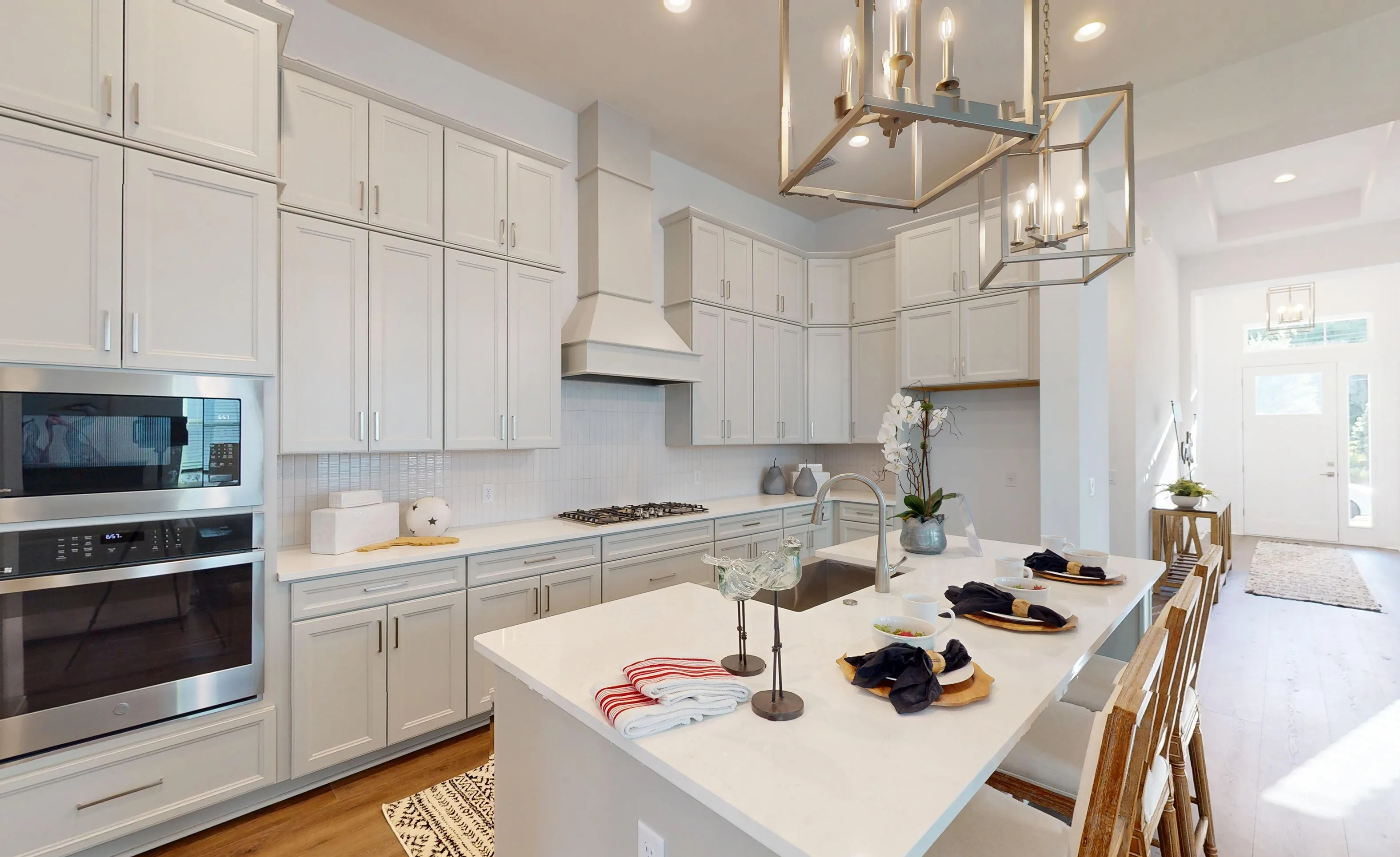 Kona plan kitchen featuring white cabinetry, a center island with quartz countertops, stainless steel appliances, and lighting.