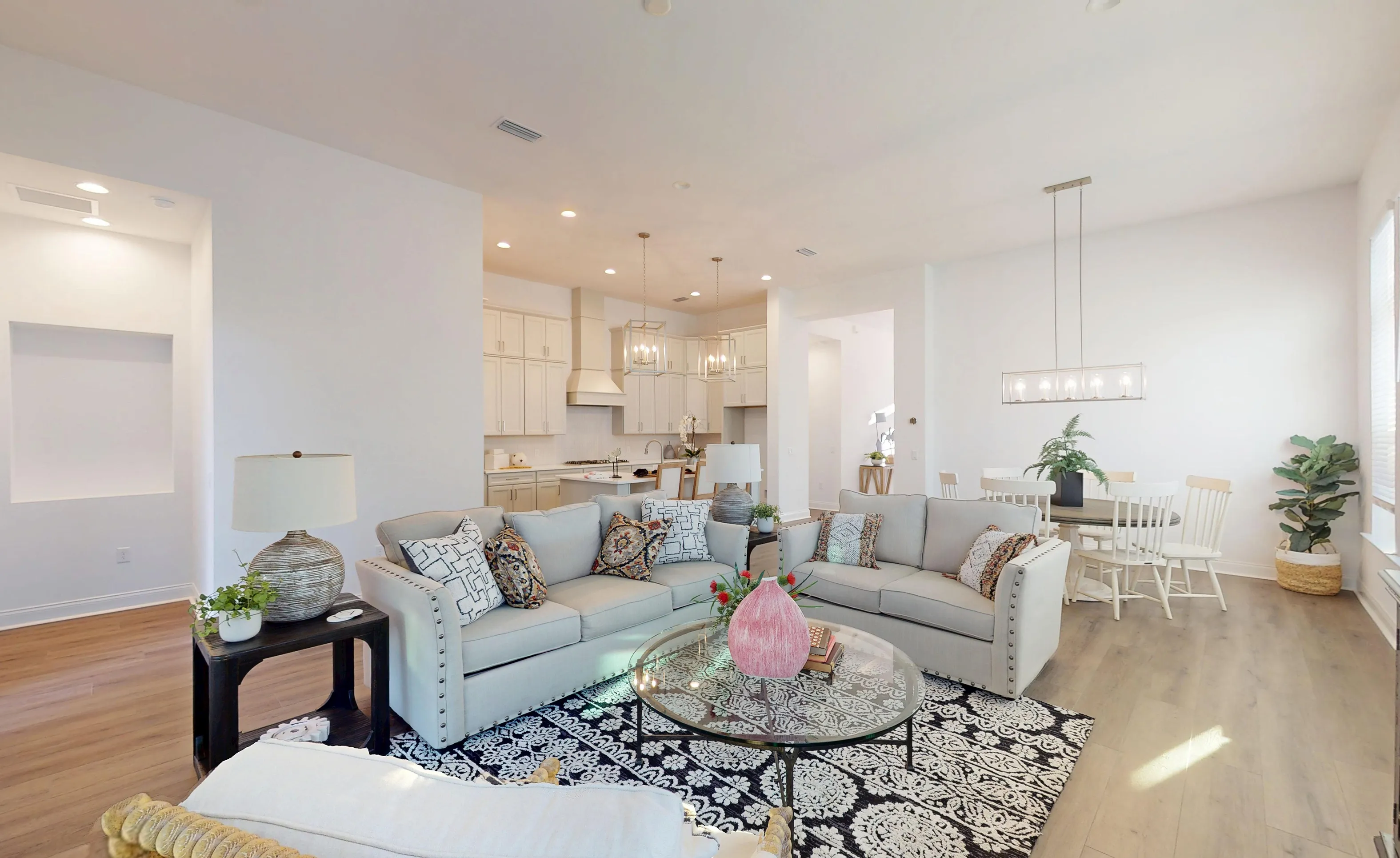 Open-concept living room in the Kona plan featuring light sofas, a glass coffee table, and an adjacent kitchen.