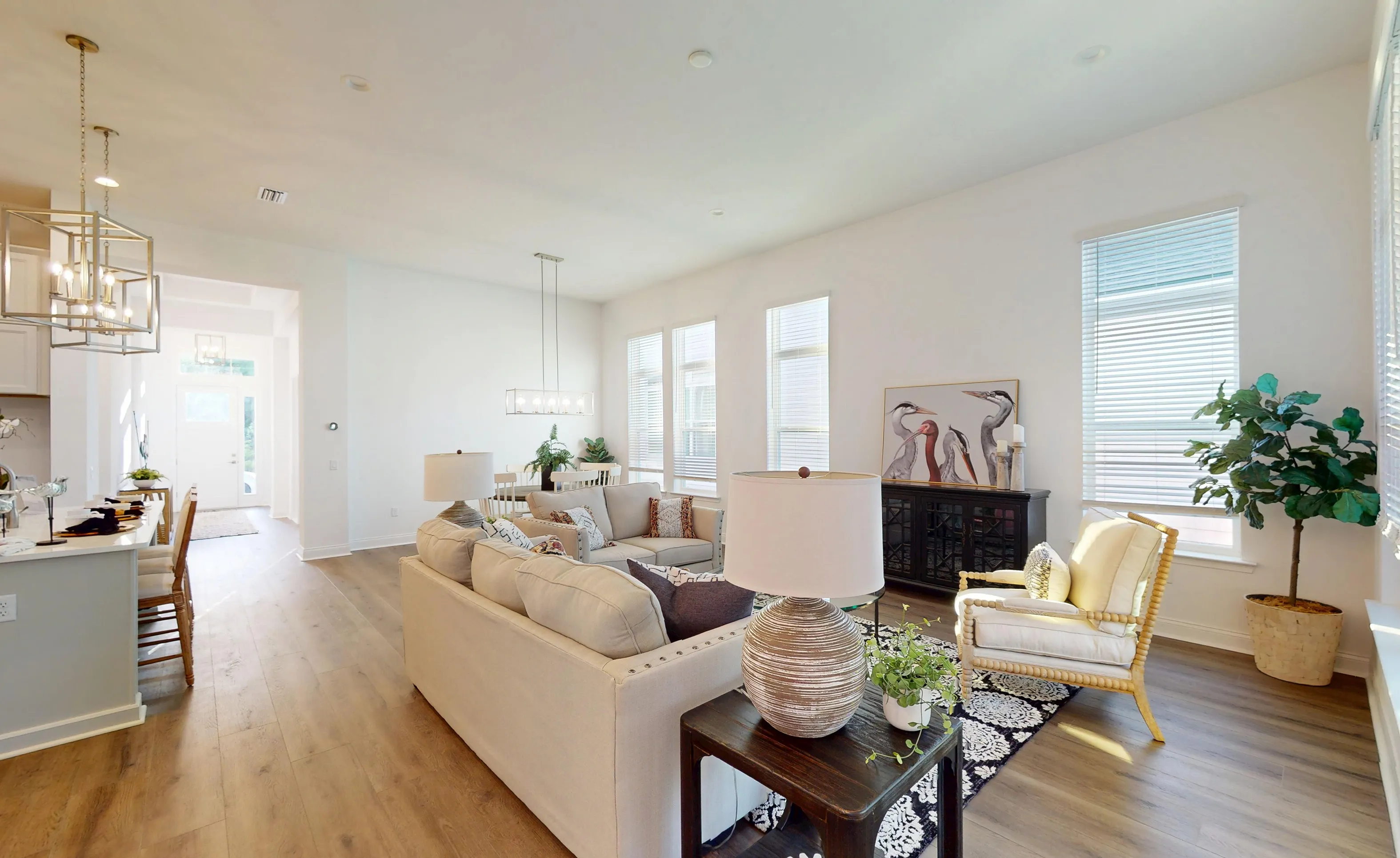 Living room of the Kona plan at Oakmont with white walls, light wood-style flooring, a beige sofa, and tall windows.