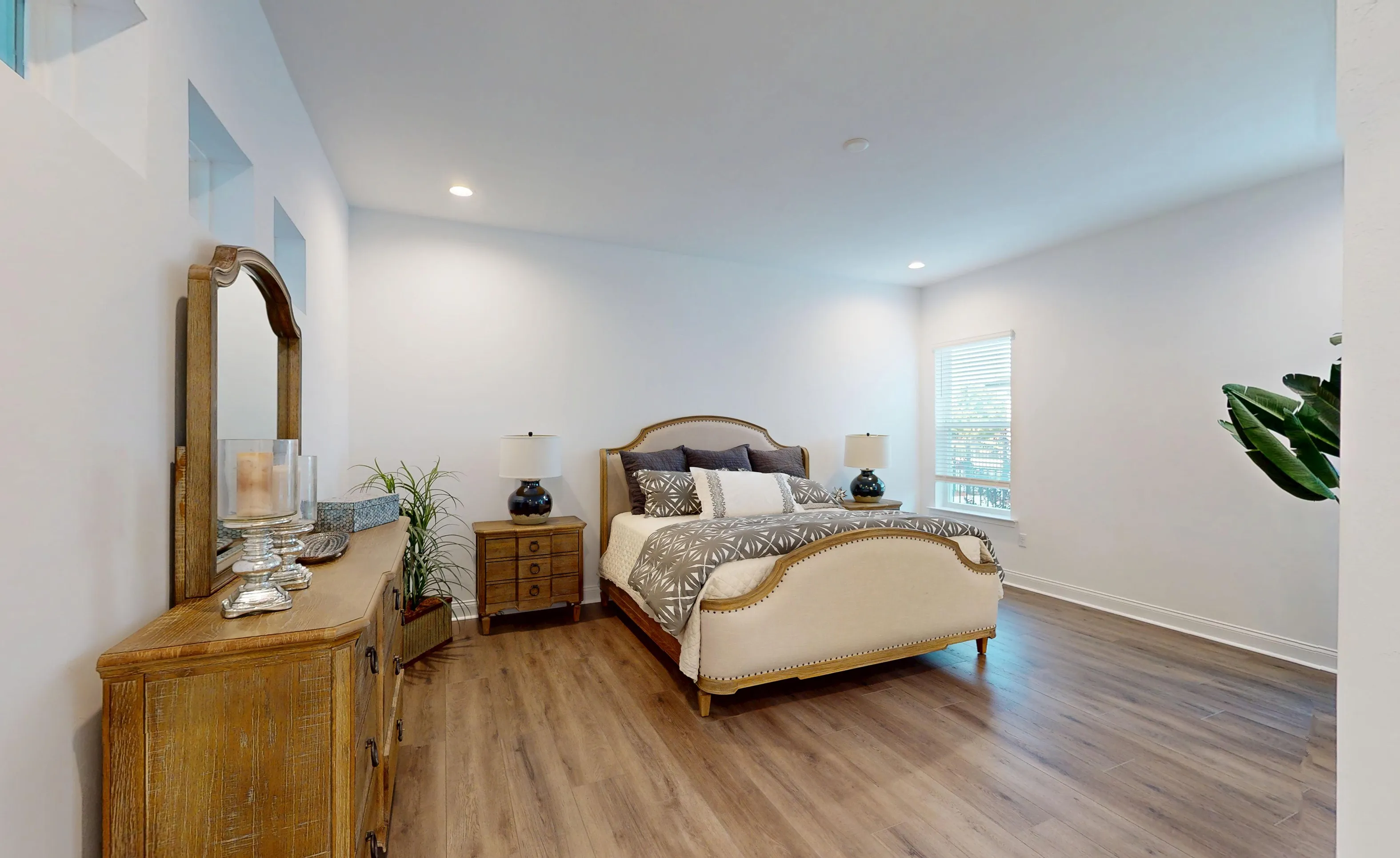 Primary bedroom in the Kona plan featuring wood-look flooring, a bed with a light fabric frame, and a wood dresser.