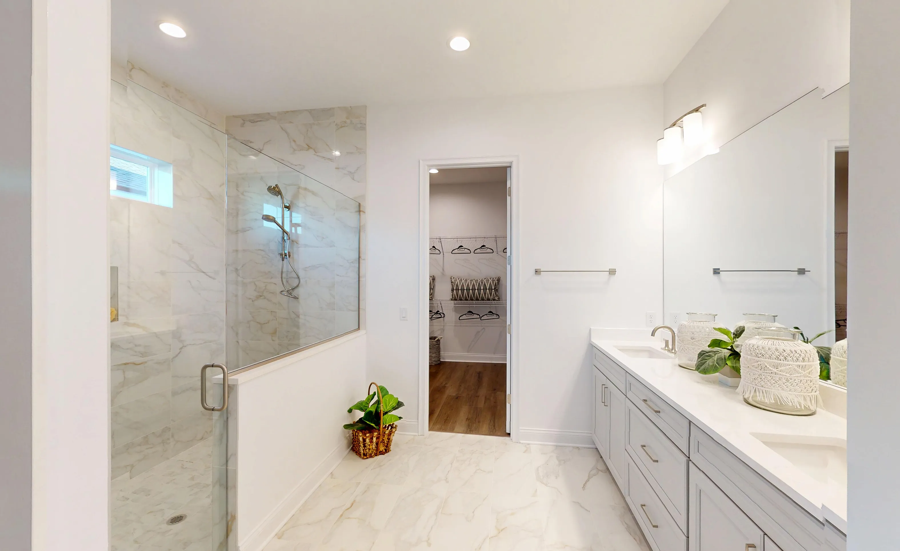 Primary bath of the Kona plan featuring a glass-enclosed shower with marble-look tile, double vanity, and walk-in closet.