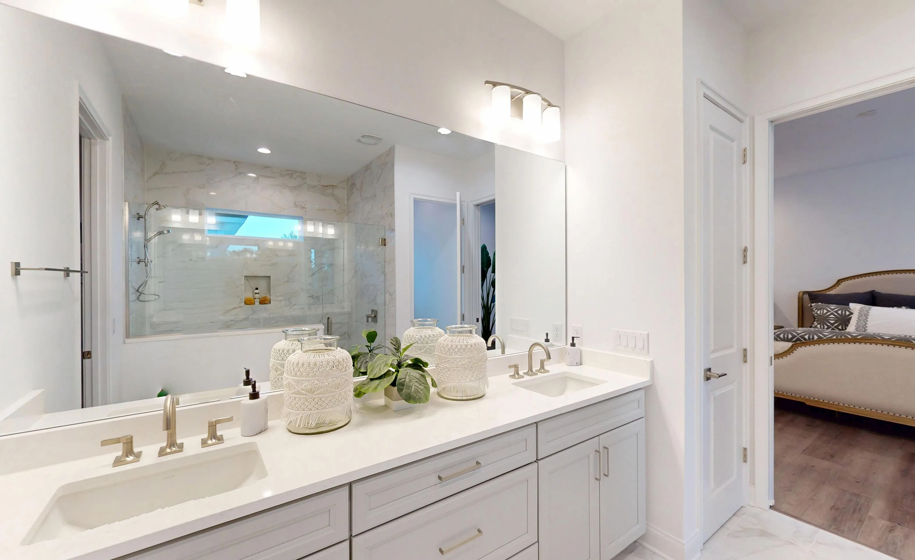 Primary bath with double vanity, quartz countertop, glass-enclosed shower, and a doorway leading to a bedroom.