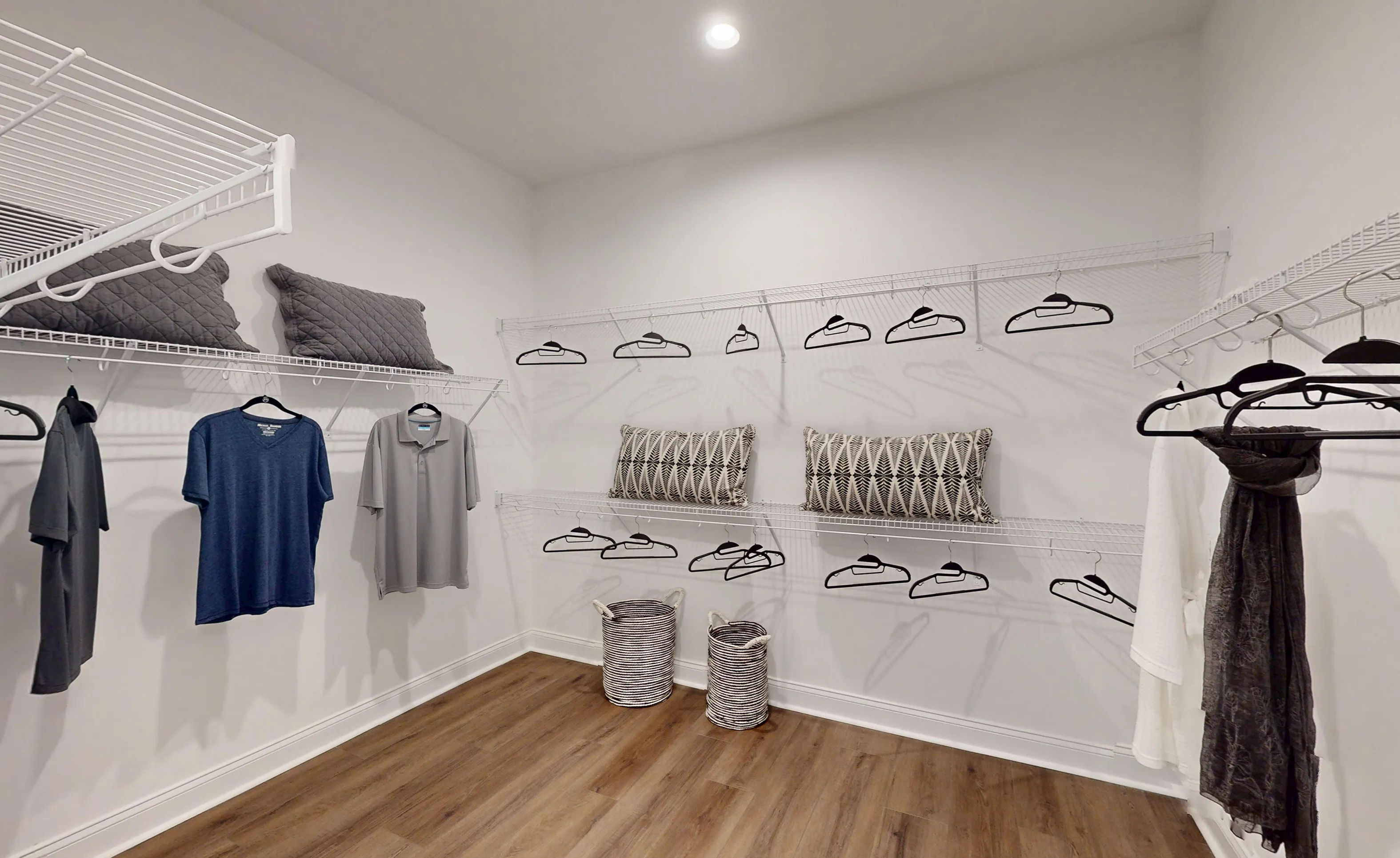 Walk-in closet in the Kona plan featuring white wire shelving, wood-look flooring, and hanging clothes.