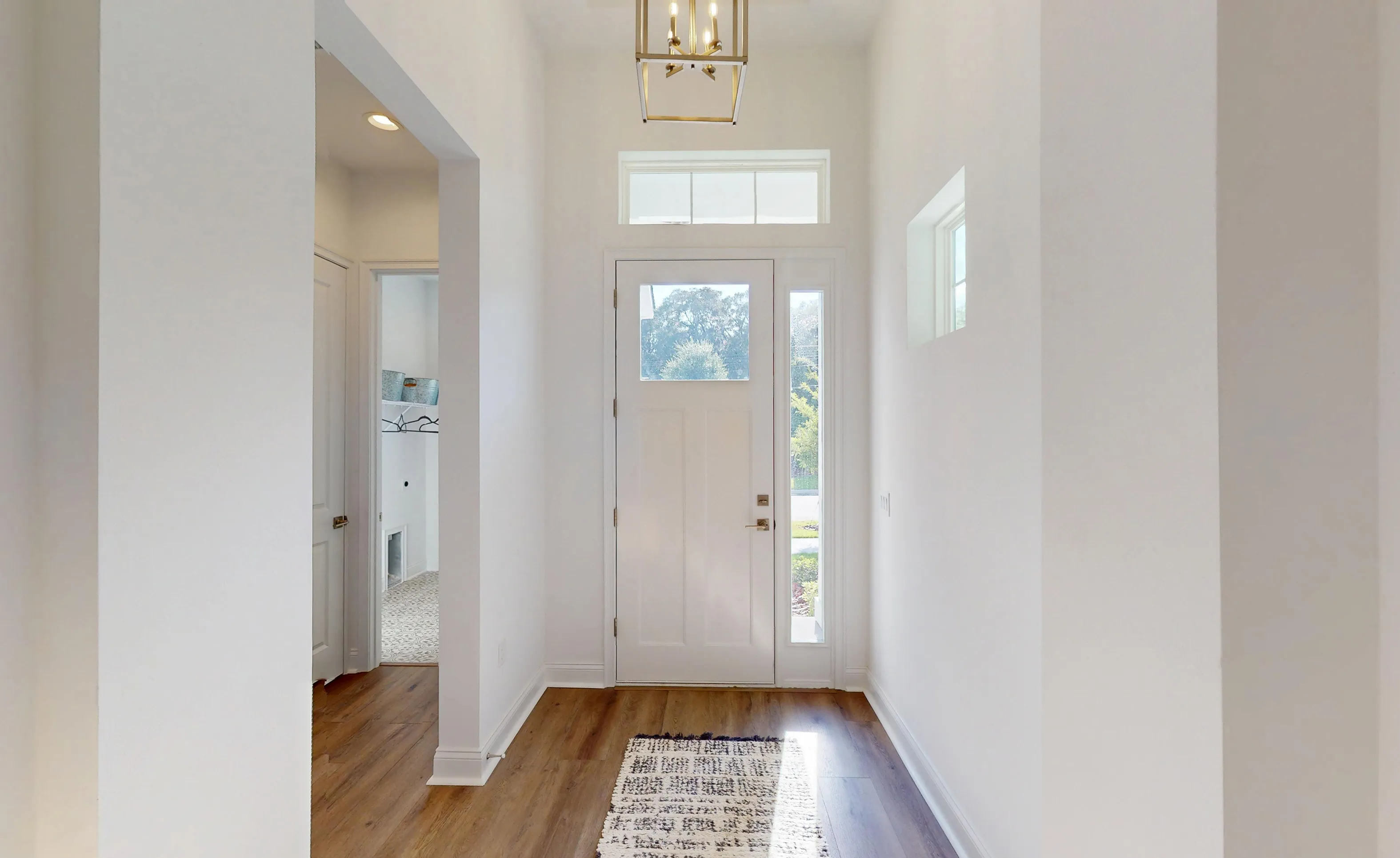 Foyer of the Kona plan featuring white walls, wood-look flooring, a white front door with sidelight, and geometric lighting.