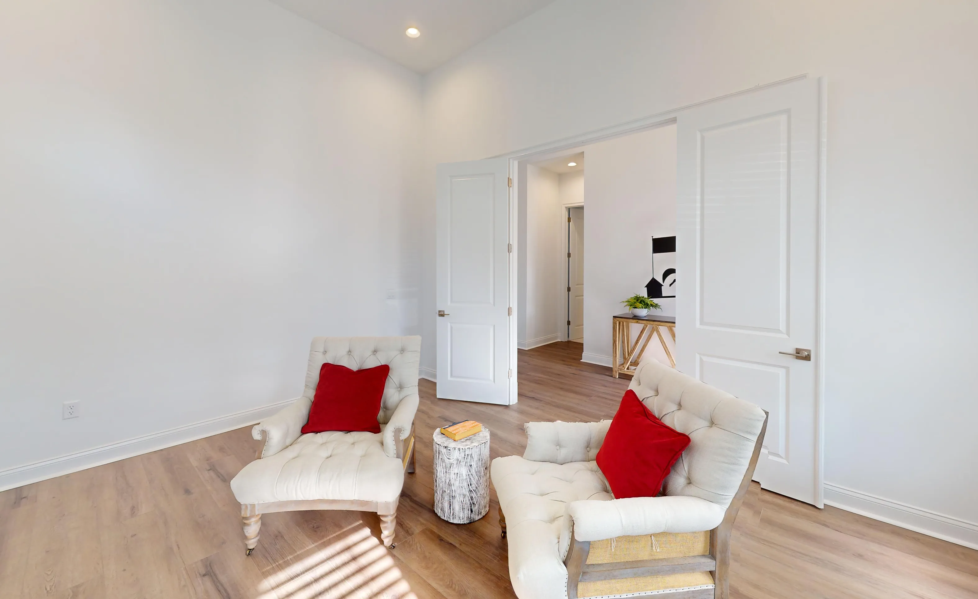 Home office in the Kona plan featuring two tufted armchairs with red pillows and double doors leading to a hallway.