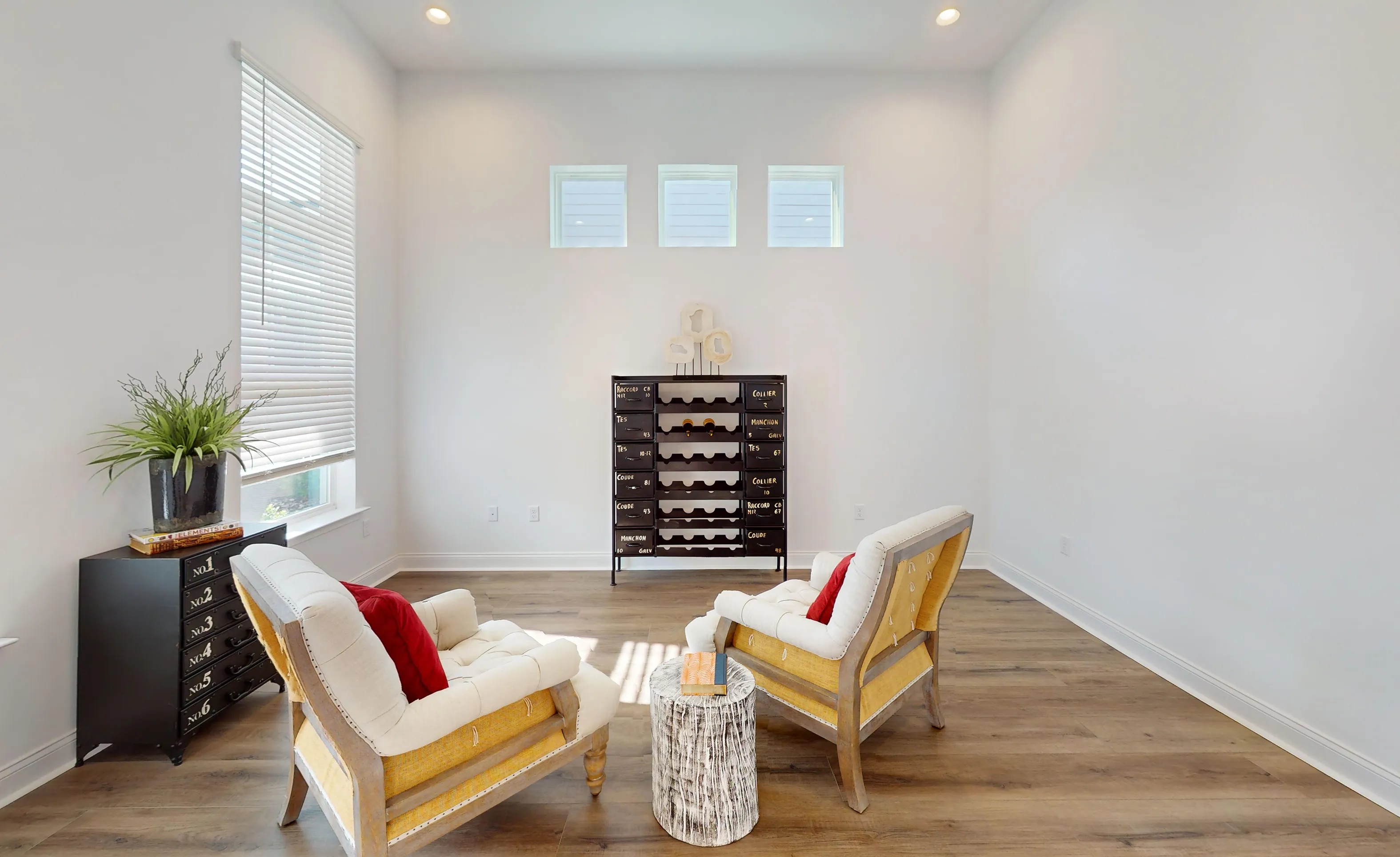 Living room in the Kona plan featuring wood-look floors, white walls, three high transom windows, and two armchairs.