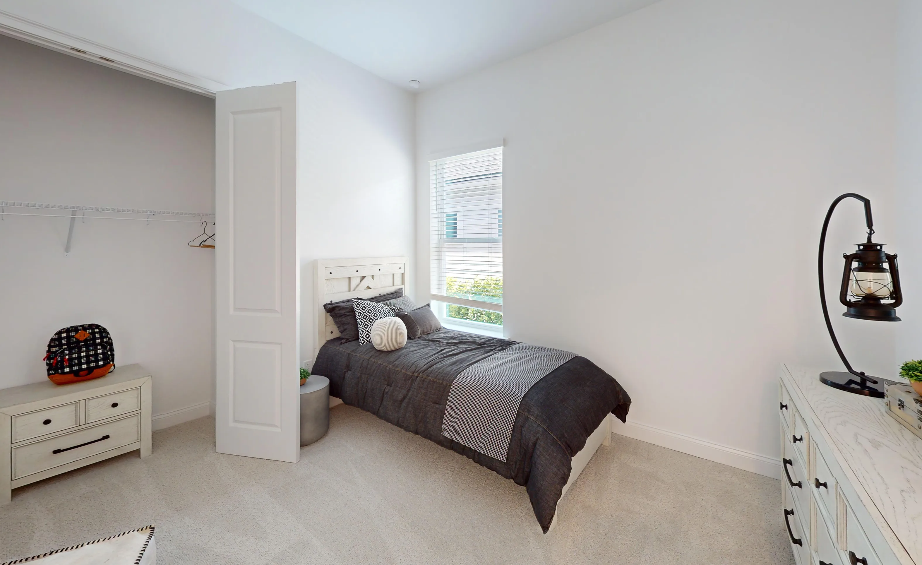 Secondary bedroom in the Kona plan with a single bed, white walls, carpeted floors, a window, and a closet with open door.