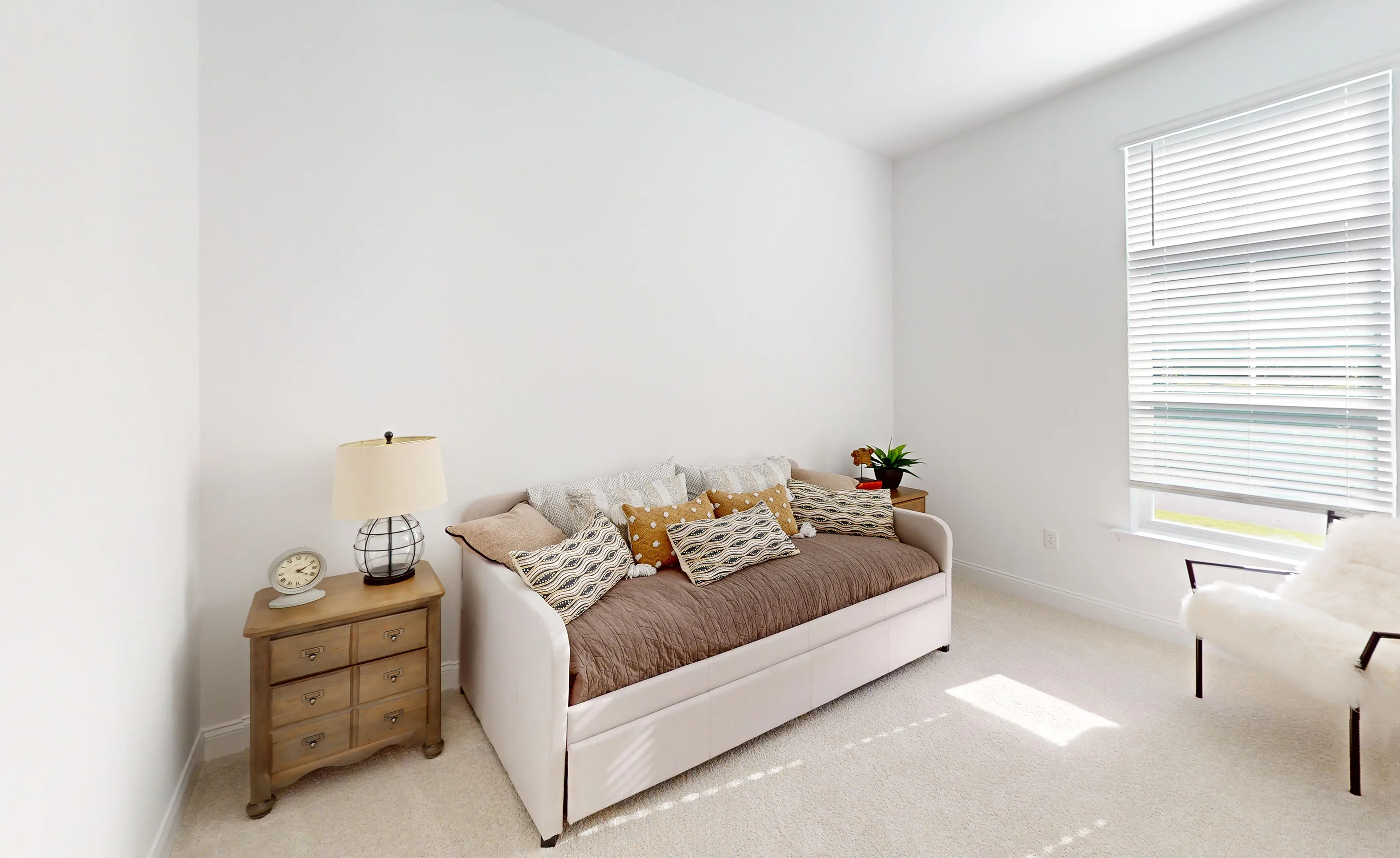 Secondary bedroom in the Kona plan featuring a daybed, wood nightstand with lamp, and window with white blinds.