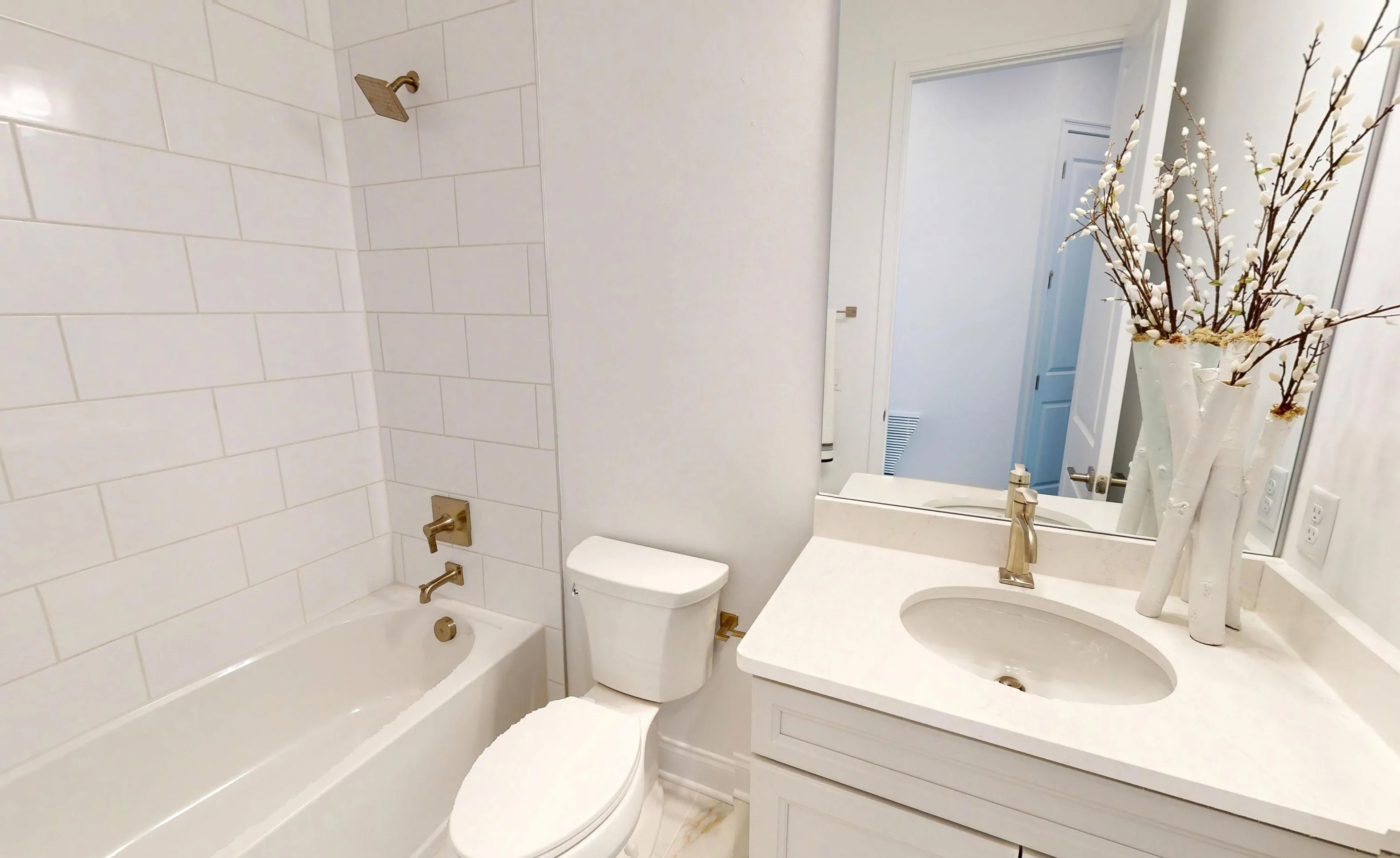 Secondary bath in Kona plan with white subway tile tub surround, gold fixtures, white vanity, and large wall mirror.