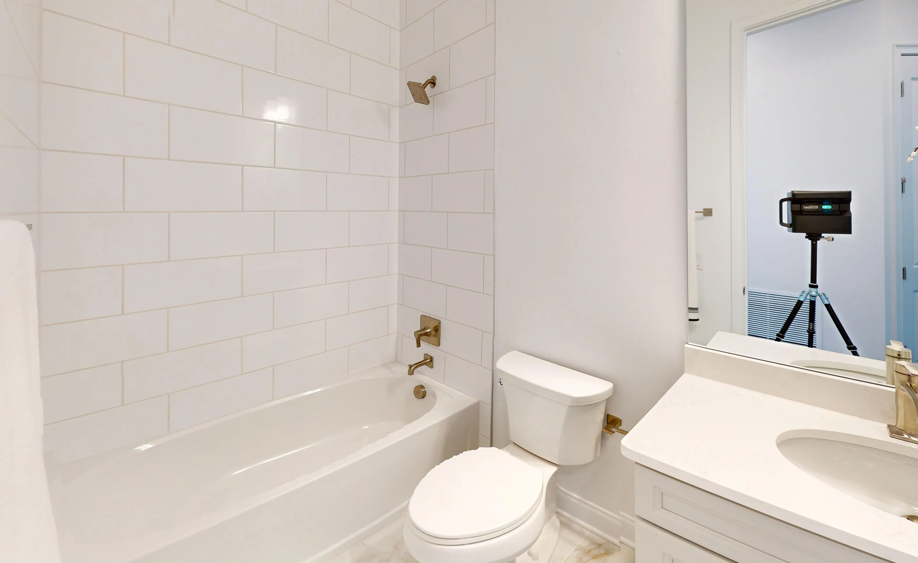 Secondary bath with a tub-shower combination featuring white subway tile, brass fixtures, and a white vanity with sink.