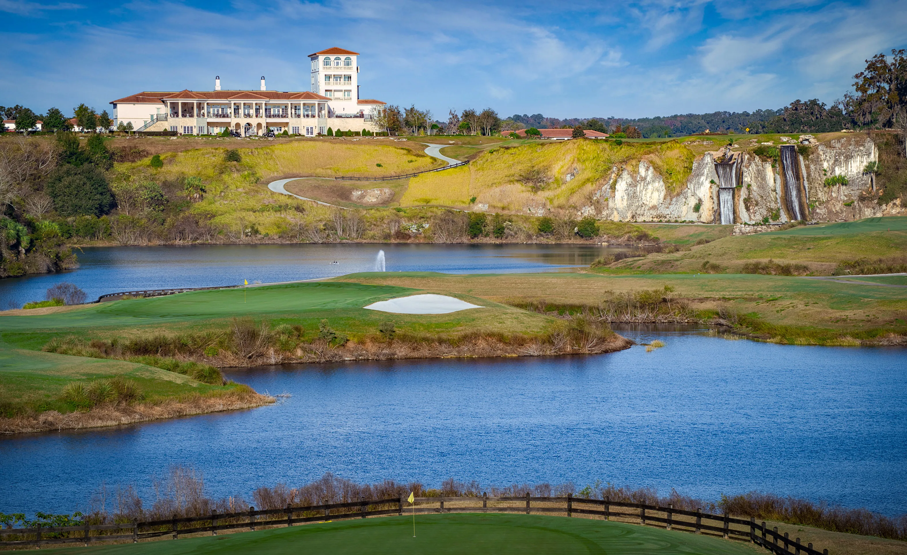 View of the IronCrest community golf course featuring a clubhouse, large lake, waterfalls on a rock cliff, and greens.