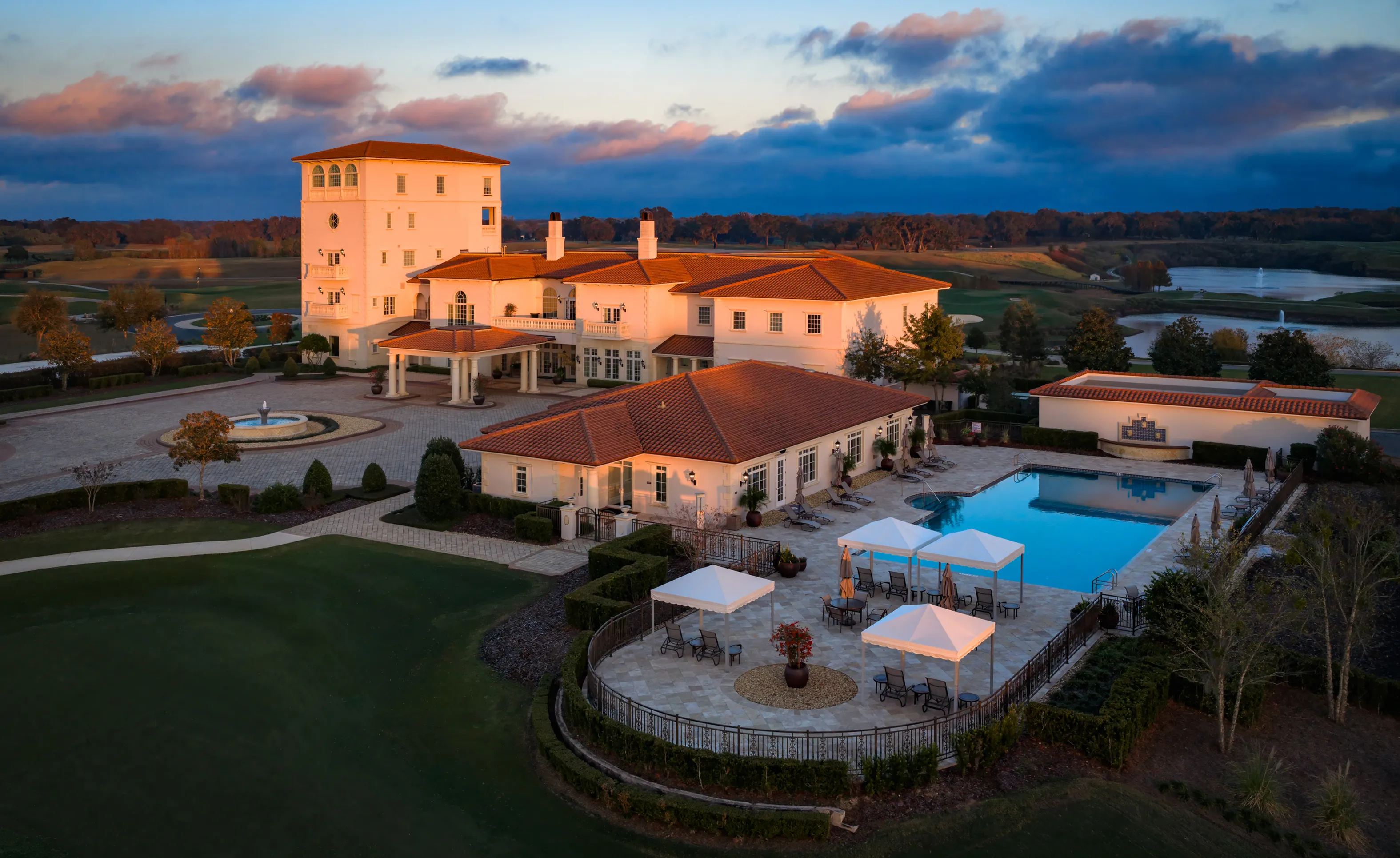 Aerial view of the IronCrest clubhouse at sunset with a tiled-roof building, large swimming pool, and stone patio.