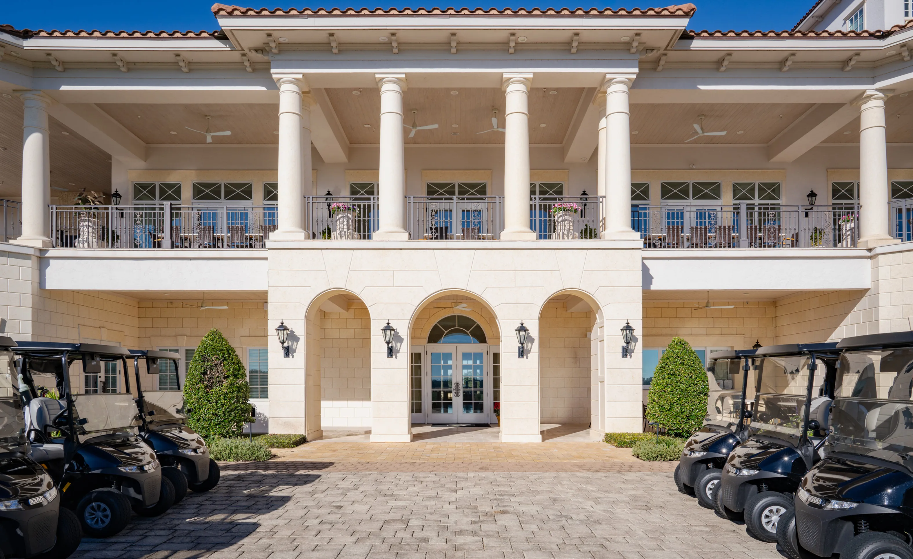 Exterior view of the IronCrest community clubhouse featuring stone arches, large white columns, and a paved entrance with carts.