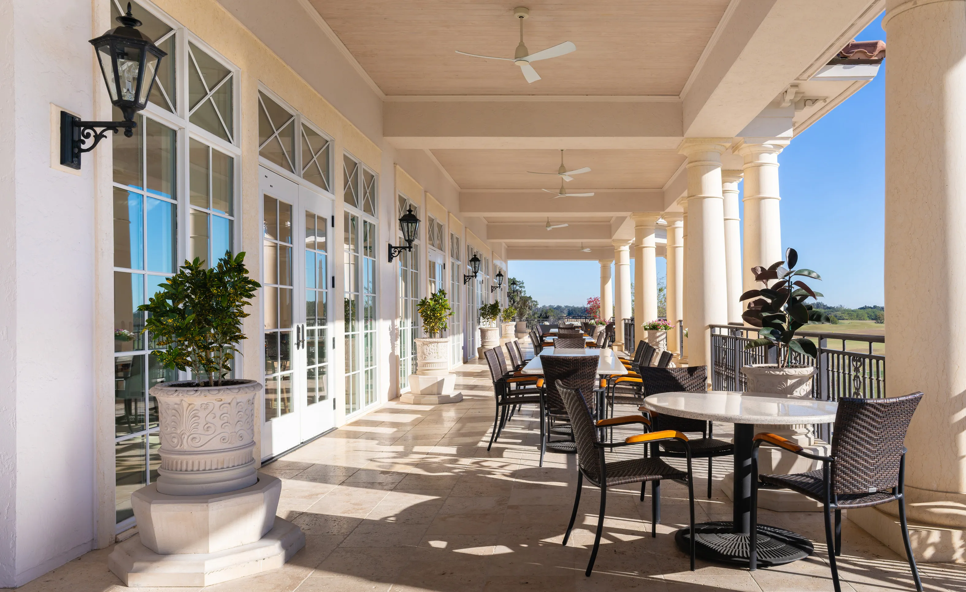 Covered patio at IronCrest with stone floors, white columns, and multiple tables with wicker chairs overlooking a golf course.