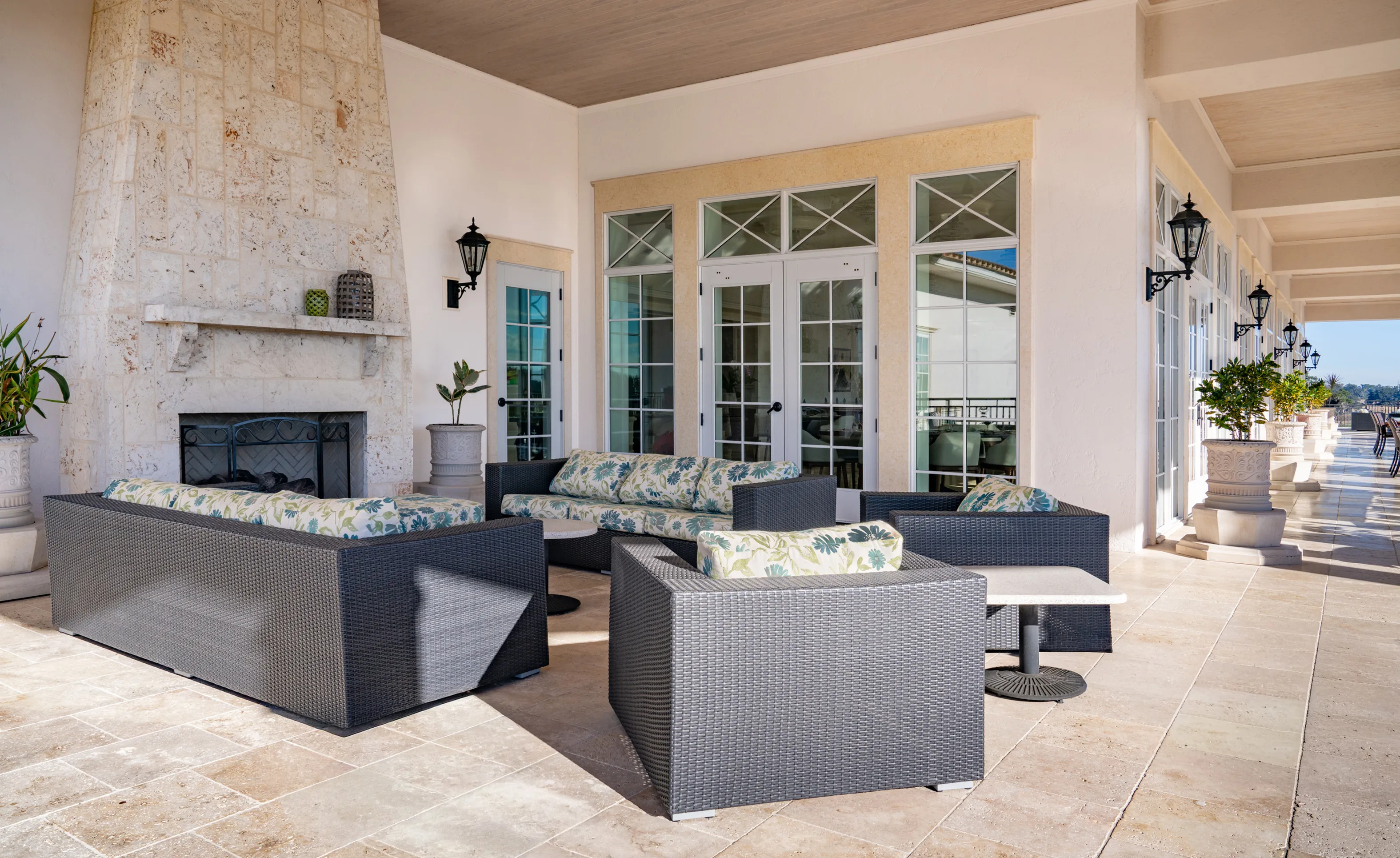 Covered patio at IronCrest with a stone fireplace, tiled flooring, wicker furniture, and glass doors.