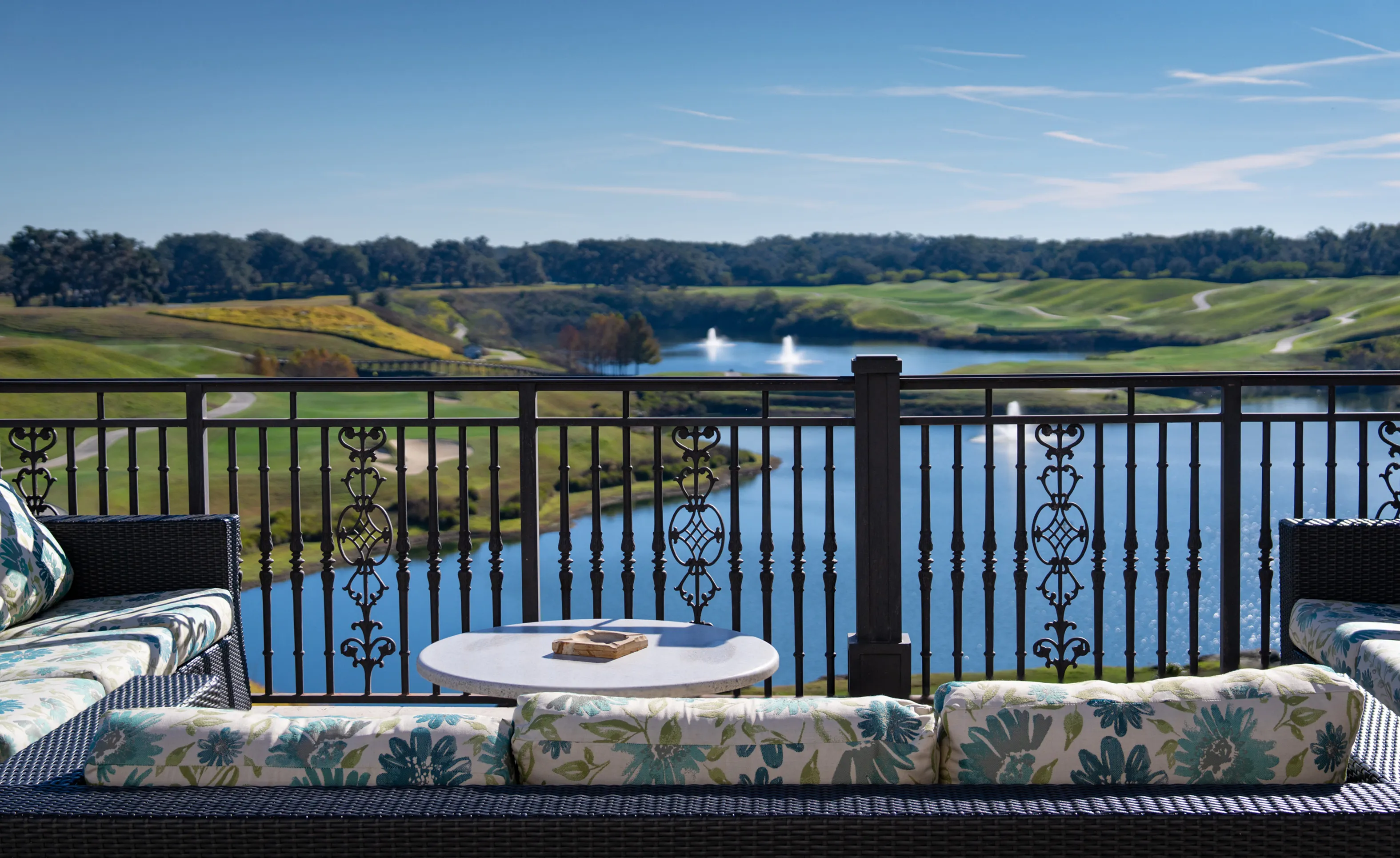Patio at IronCrest with wicker seating overlooking a lake, fountain, and golf course.