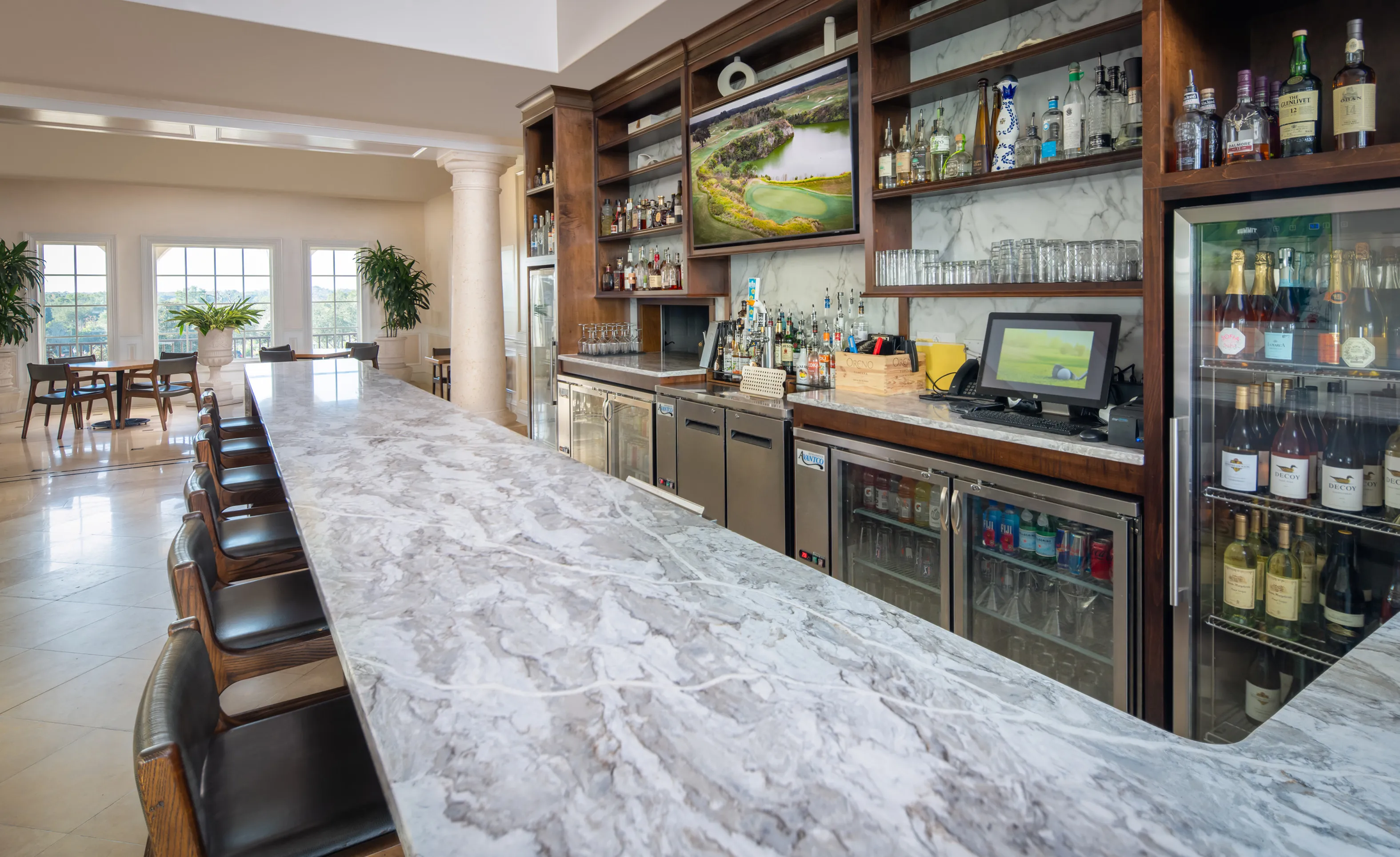 IronCrest community bar area with a long, veined marble countertop, stainless steel refrigerators, and wall shelving.