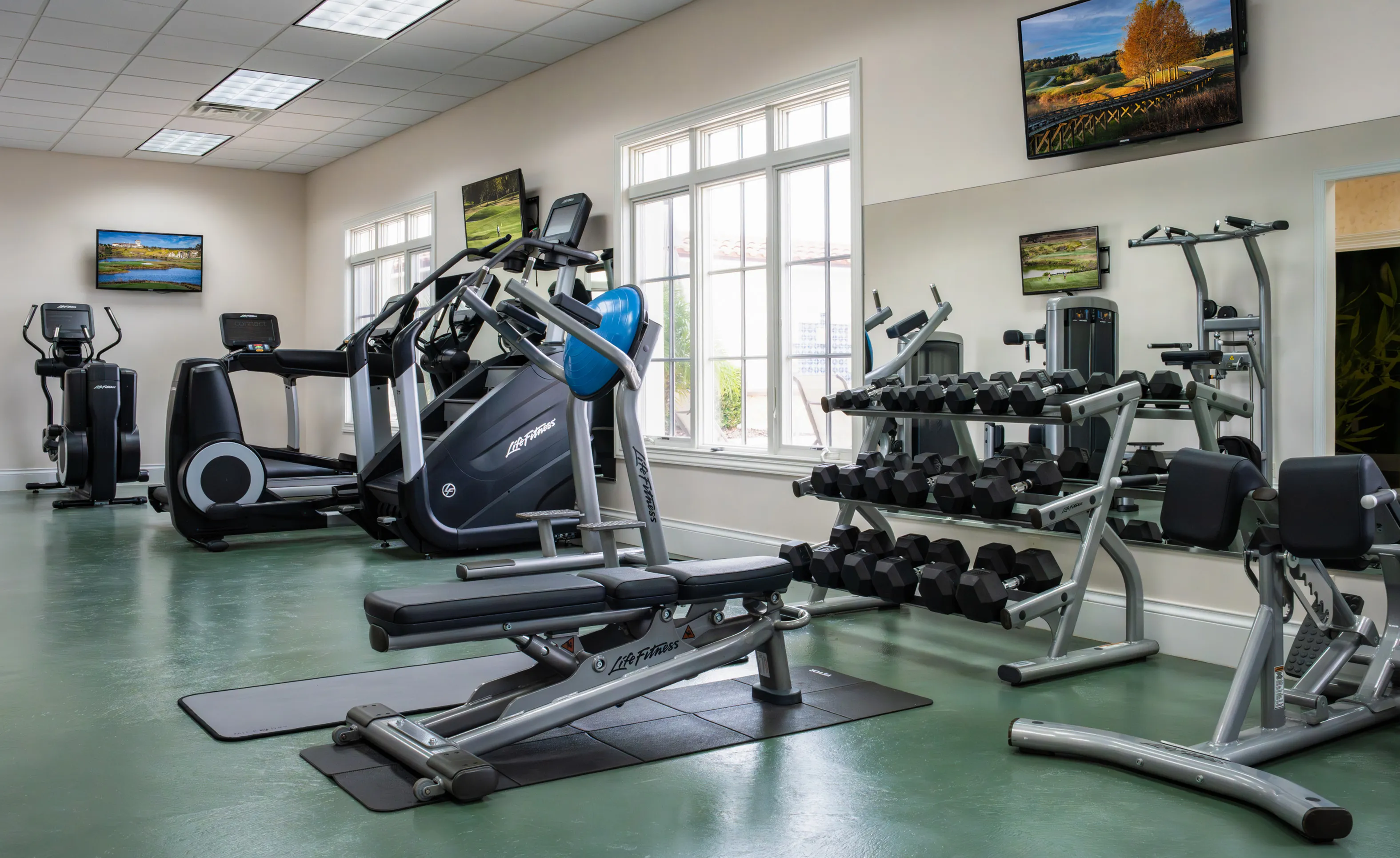 Fitness center at IronCrest with cardio machines, a weight bench, dumbbell rack, and large windows with natural light.