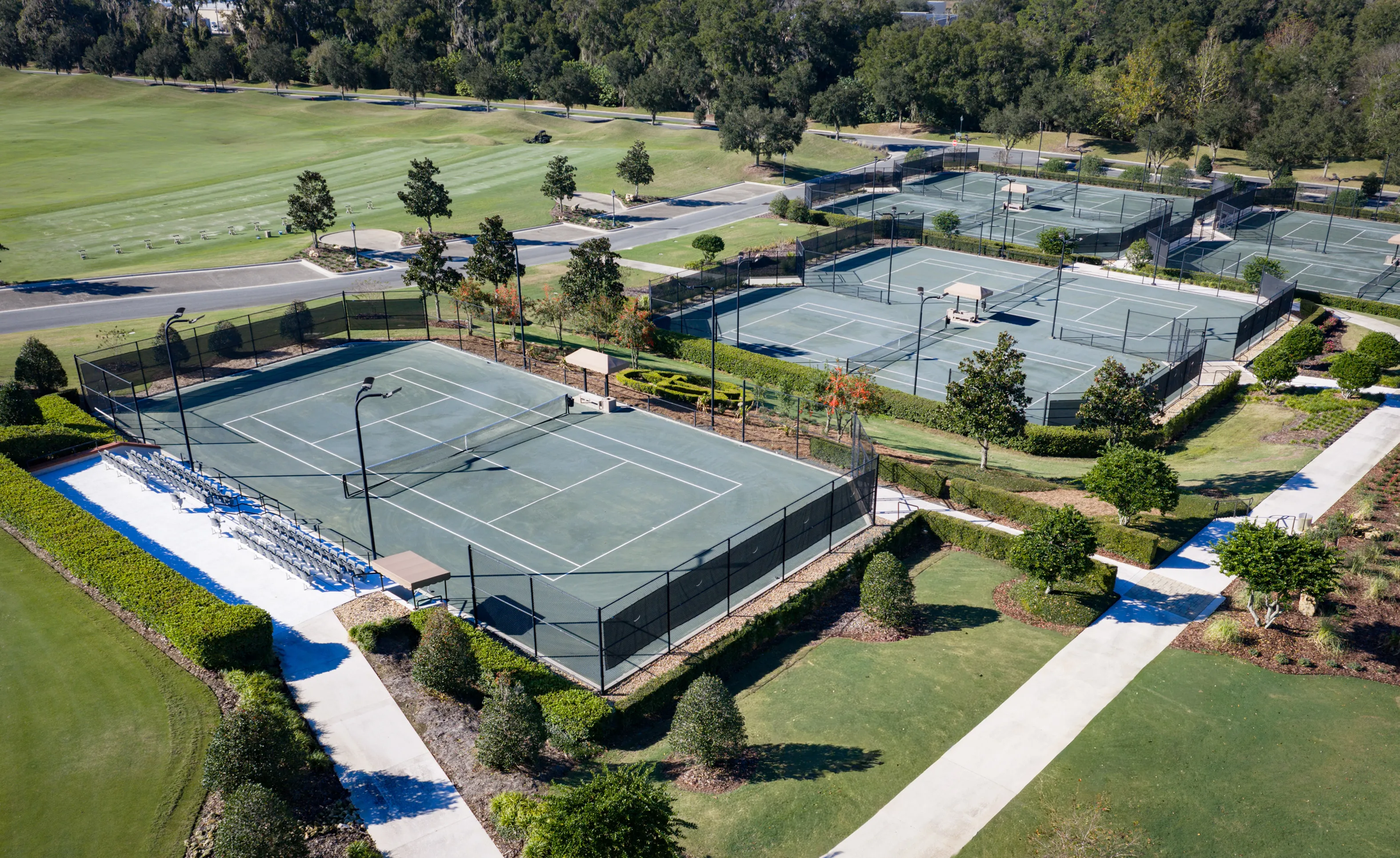 Aerial view of outdoor tennis courts with fenced boundaries, bleacher seating, and landscaped paths at IronCrest.