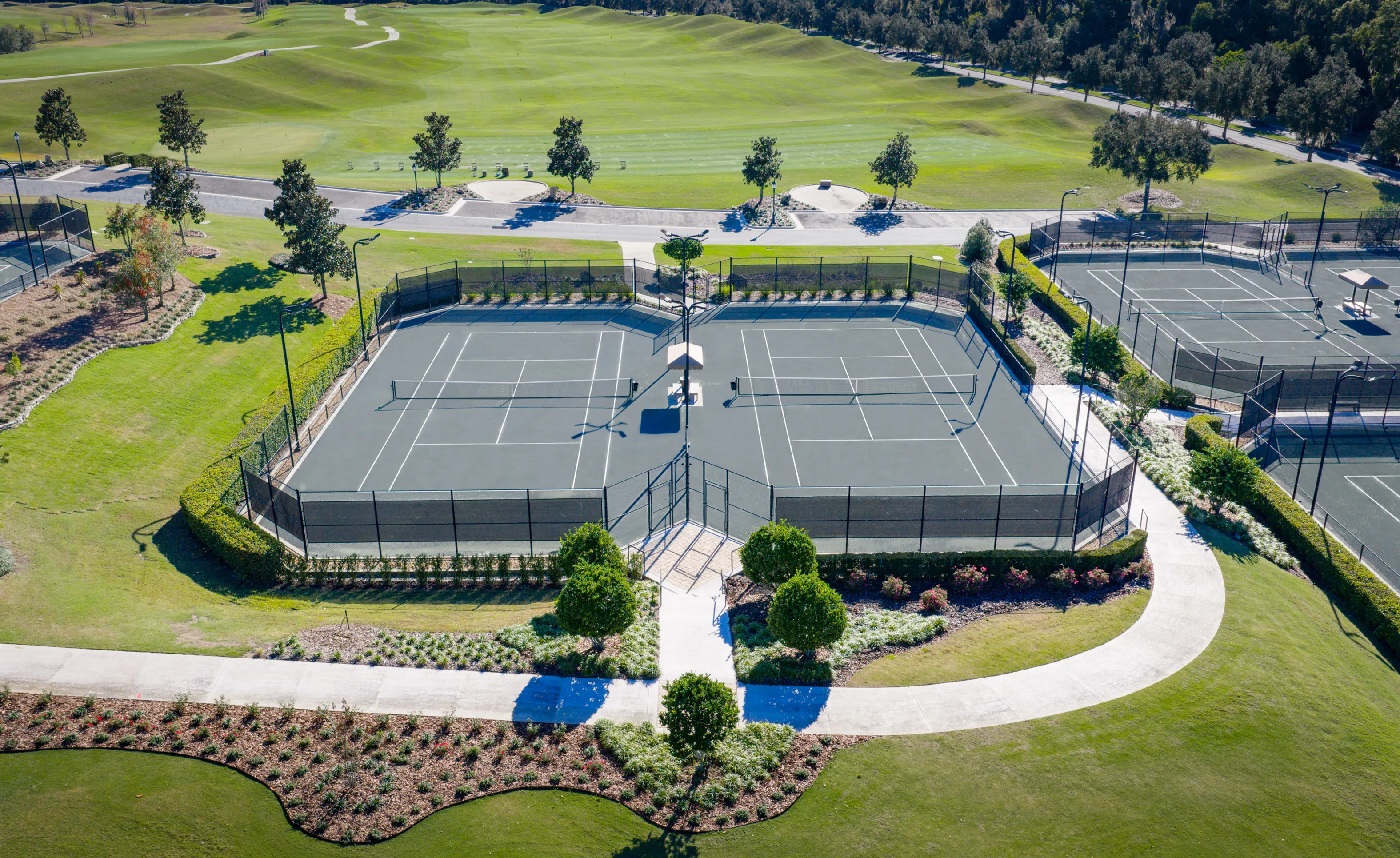 Aerial view of fenced tennis courts at IronCrest, surrounded by landscaped lawns and a golf course.