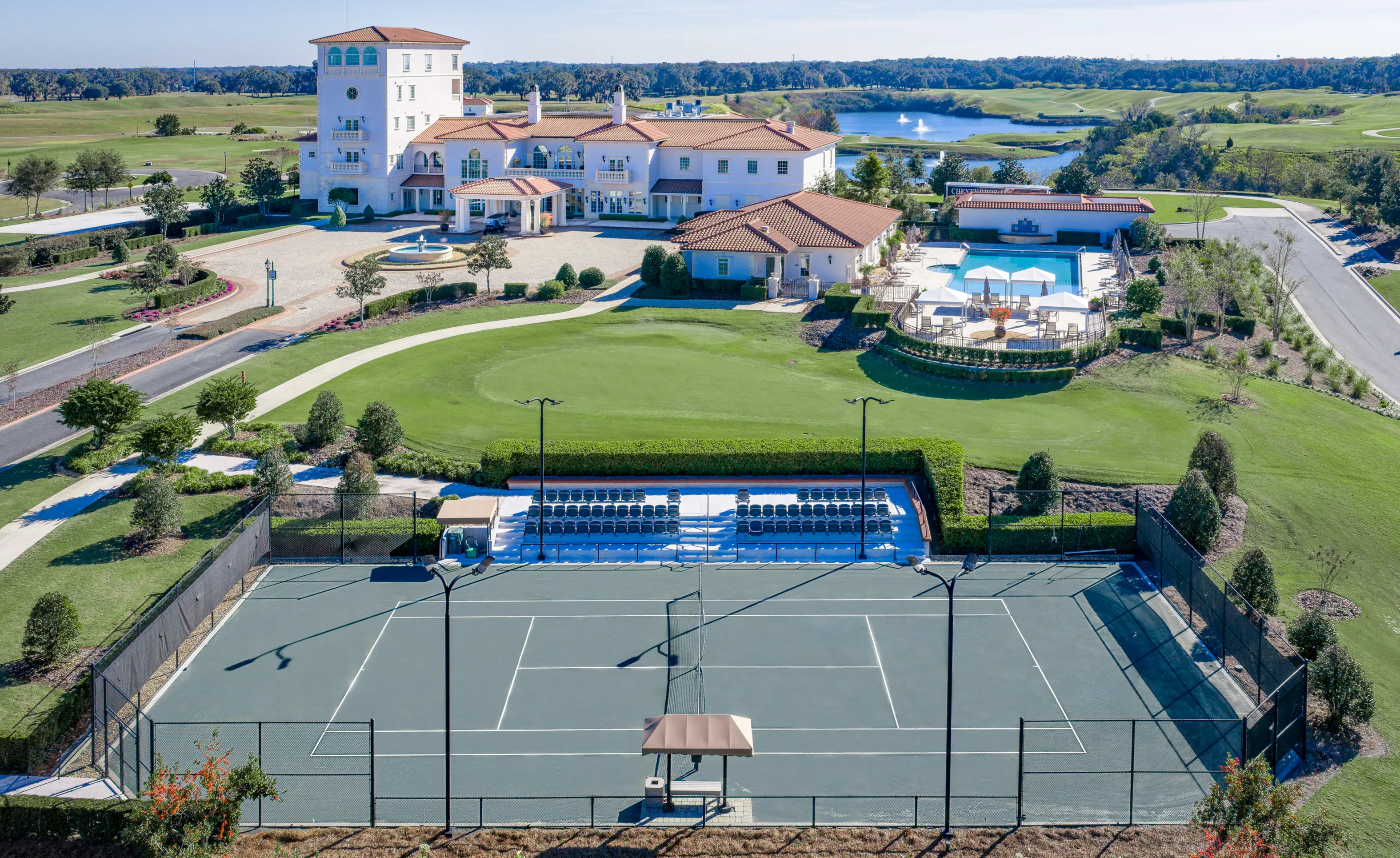 Aerial view of IronCrest community featuring a tennis court, bleachers, swimming pool, and clubhouse on a golf course.