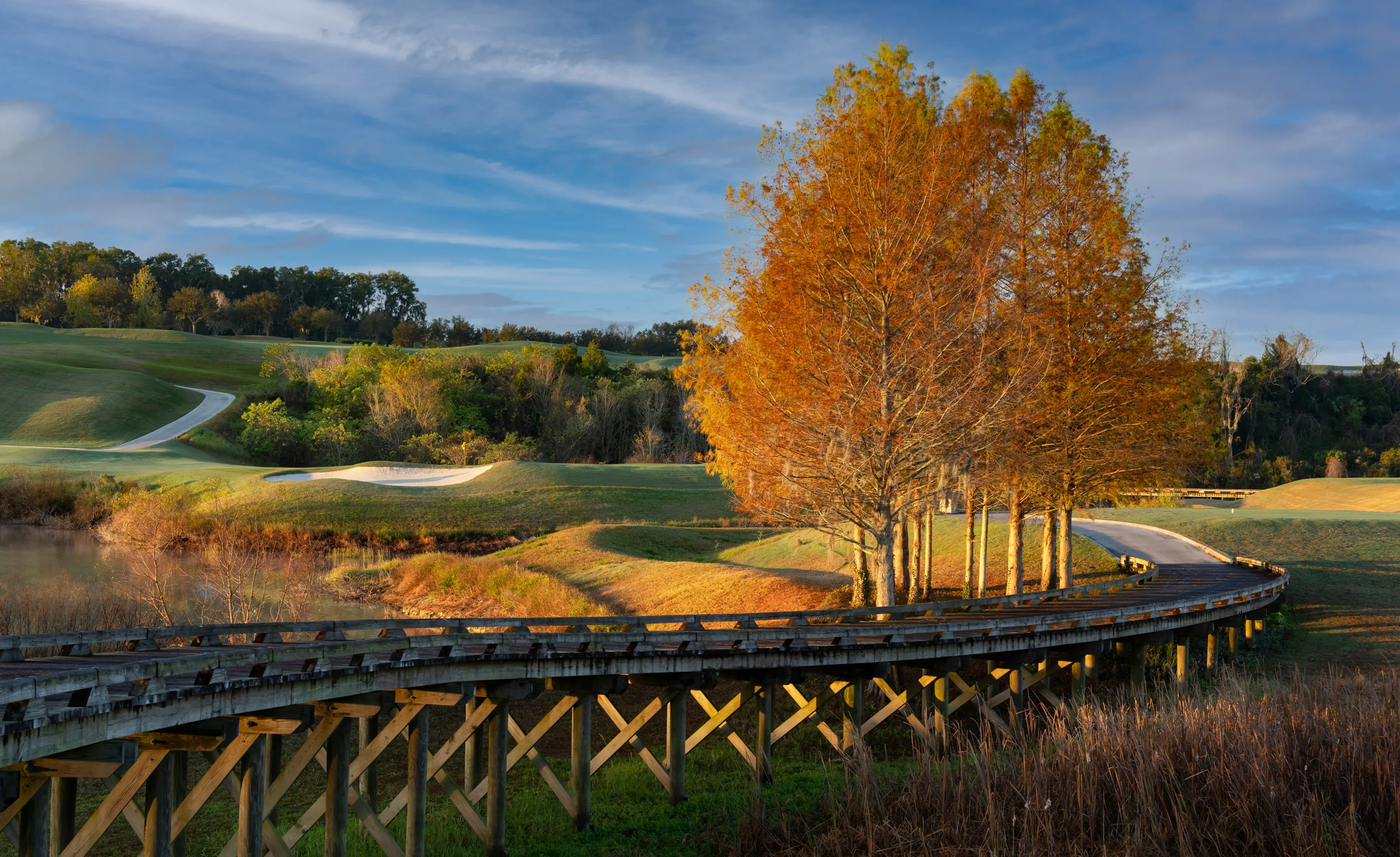 Wooden bridge winding through a golf course at IronCrest with autumn-colored trees and rolling green hills.