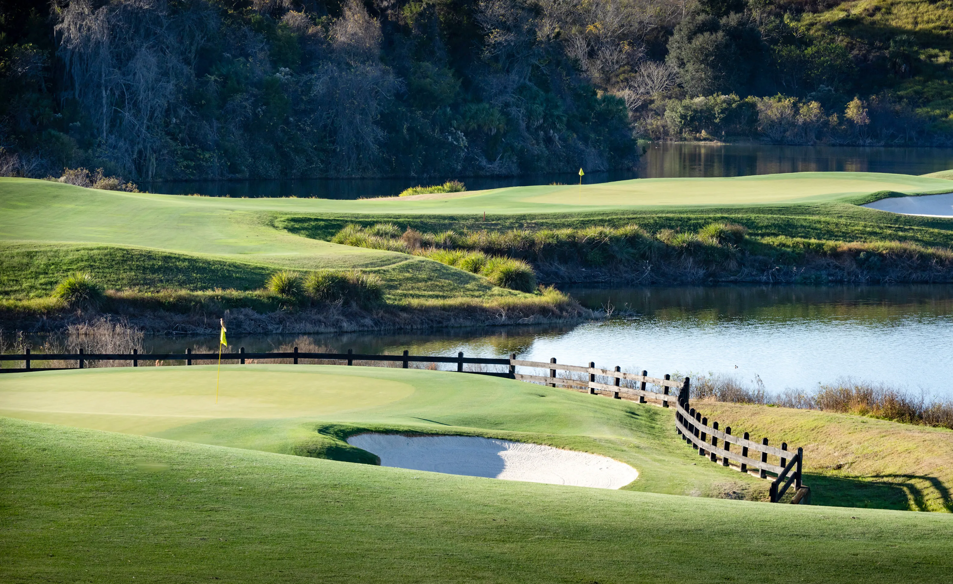 Golf course putting green with a sand bunker, a wooden fence, and a lake at the IronCrest community.