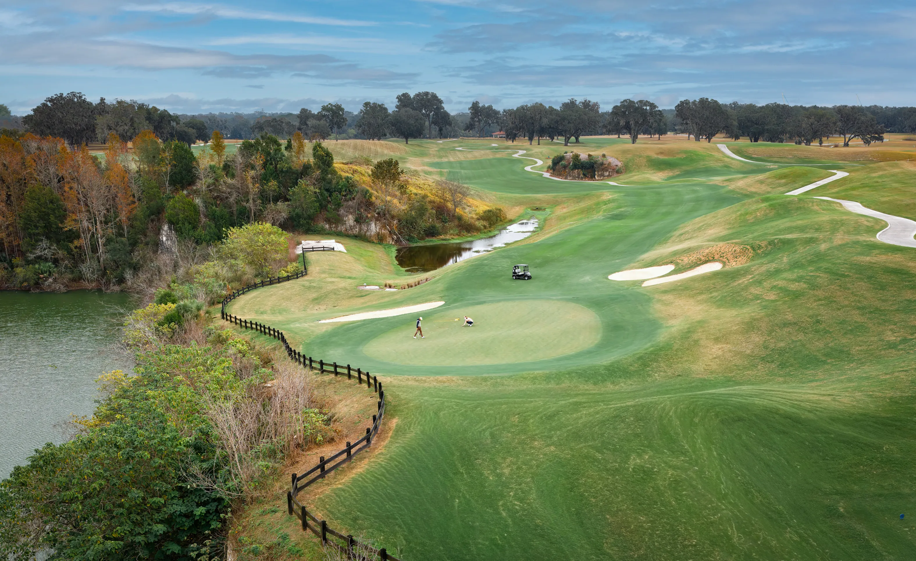 Aerial view of a sprawling IronCrest golf course with rolling green fairways, sand bunkers, a water hazard, and a golf cart.