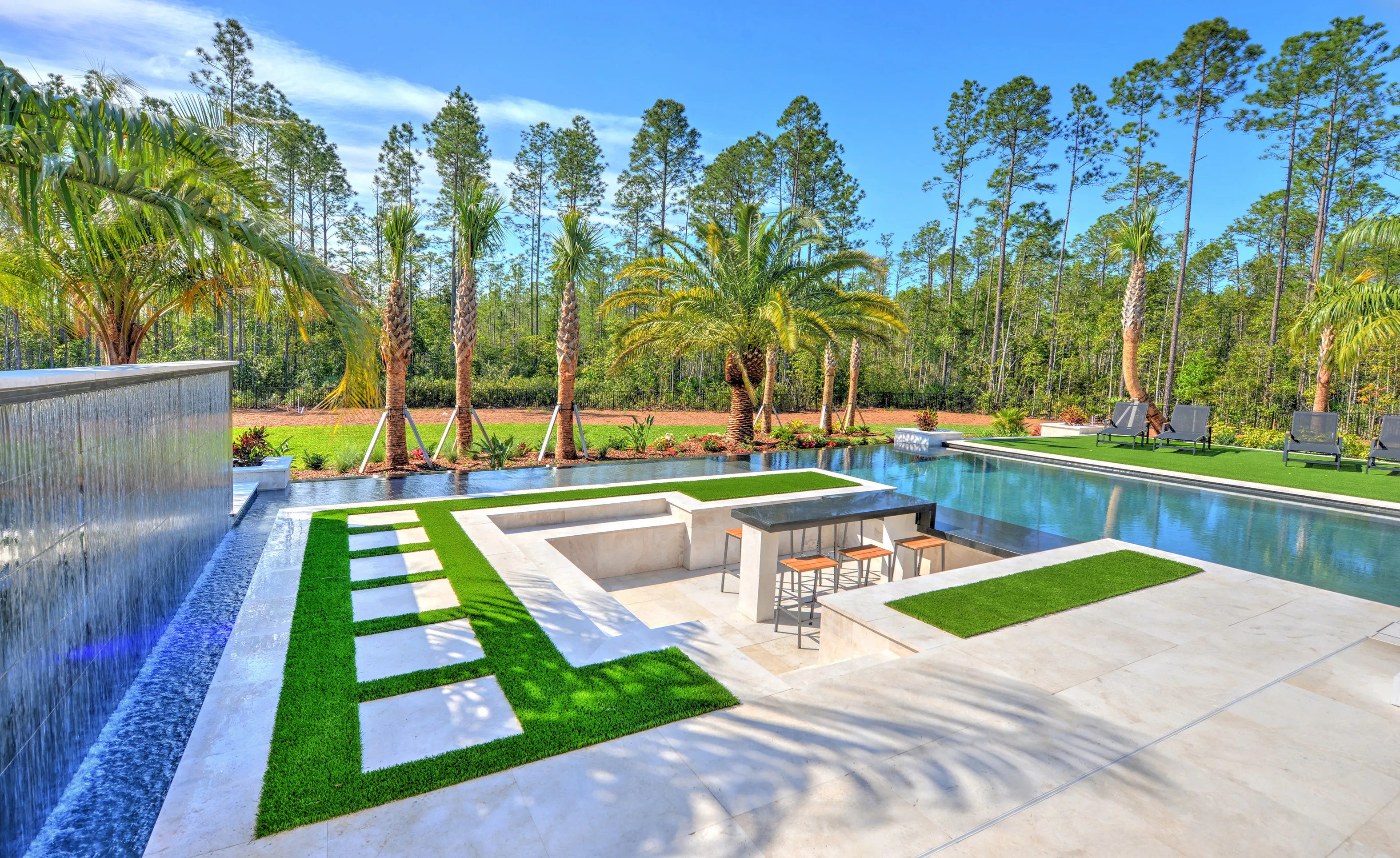 Backyard pool at Courtney Grove featuring a sunken seating area with a table, a water wall, and artificial turf lawn.