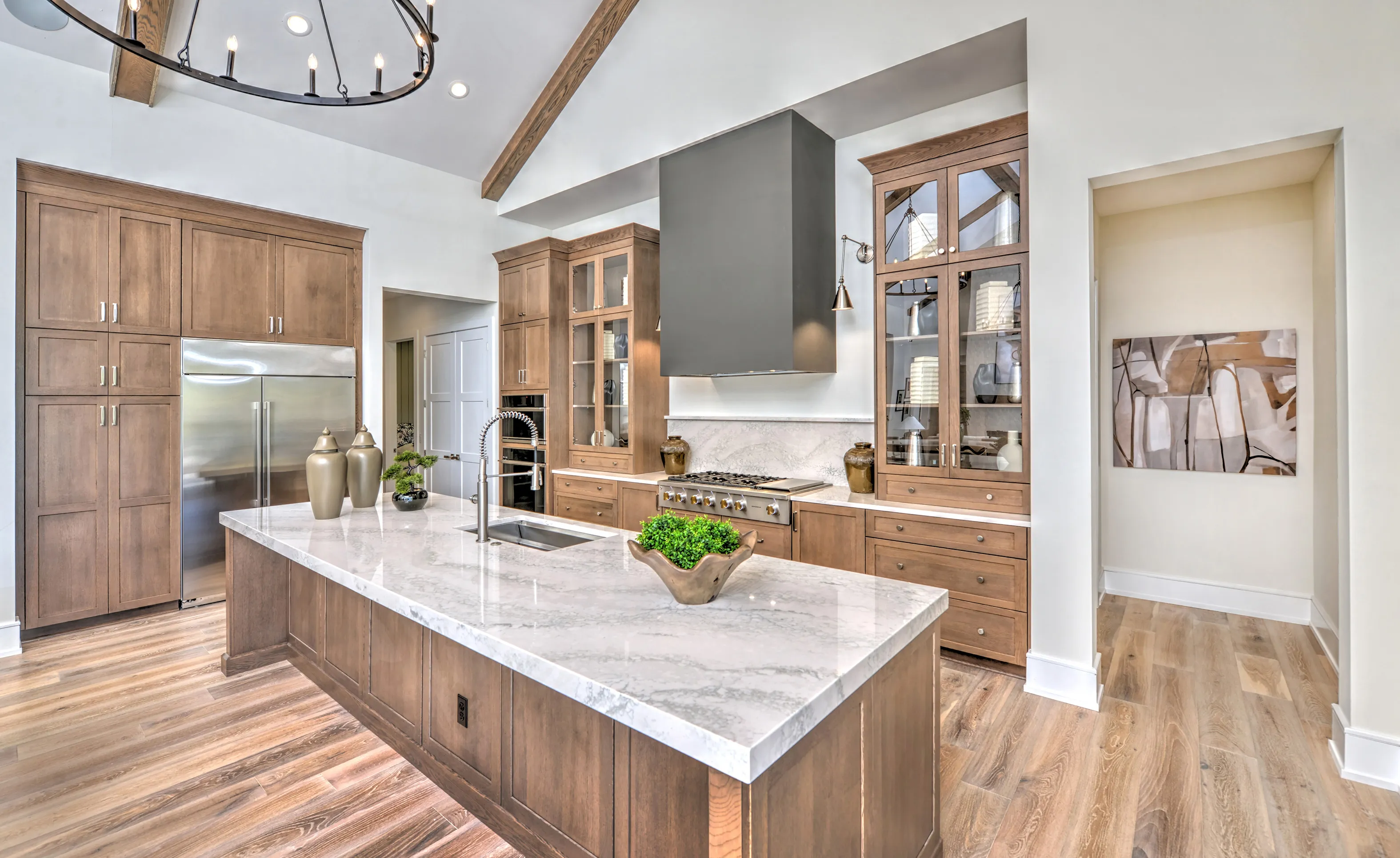 Kitchen with wood cabinets, marble island countertop, vaulted ceiling, and dark range hood in Courtney Grove home.