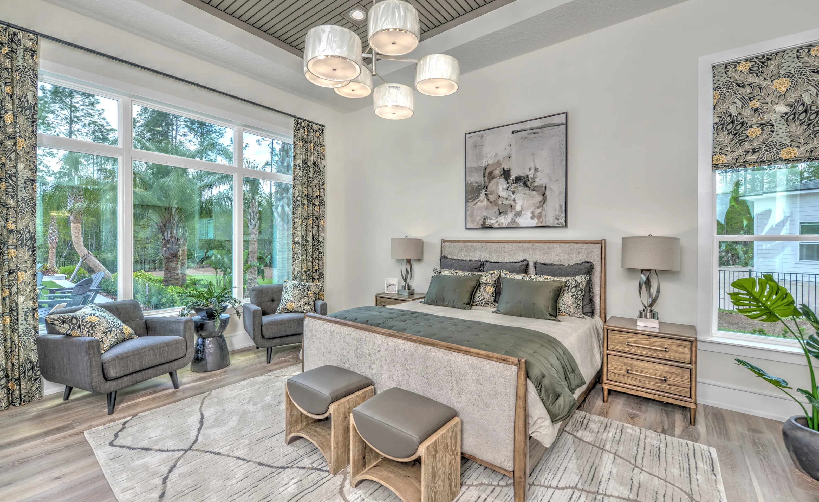 Bright bedroom in Courtney Grove with a large window, tray ceiling, upholstered bed, and two gray armchairs.