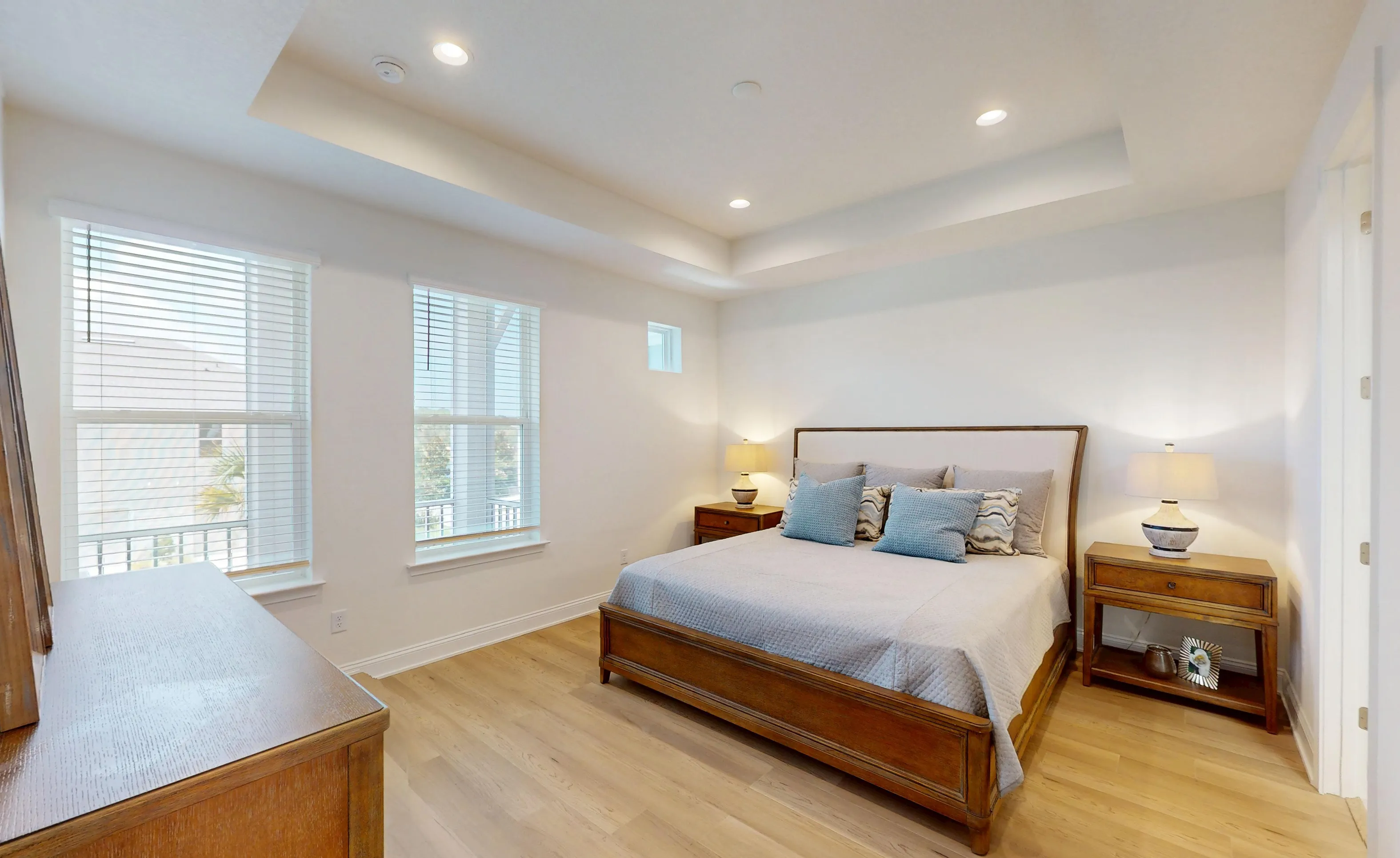 Primary bedroom in the Castillo plan featuring light wood floors, a tray ceiling with recessed lighting, and two windows.
