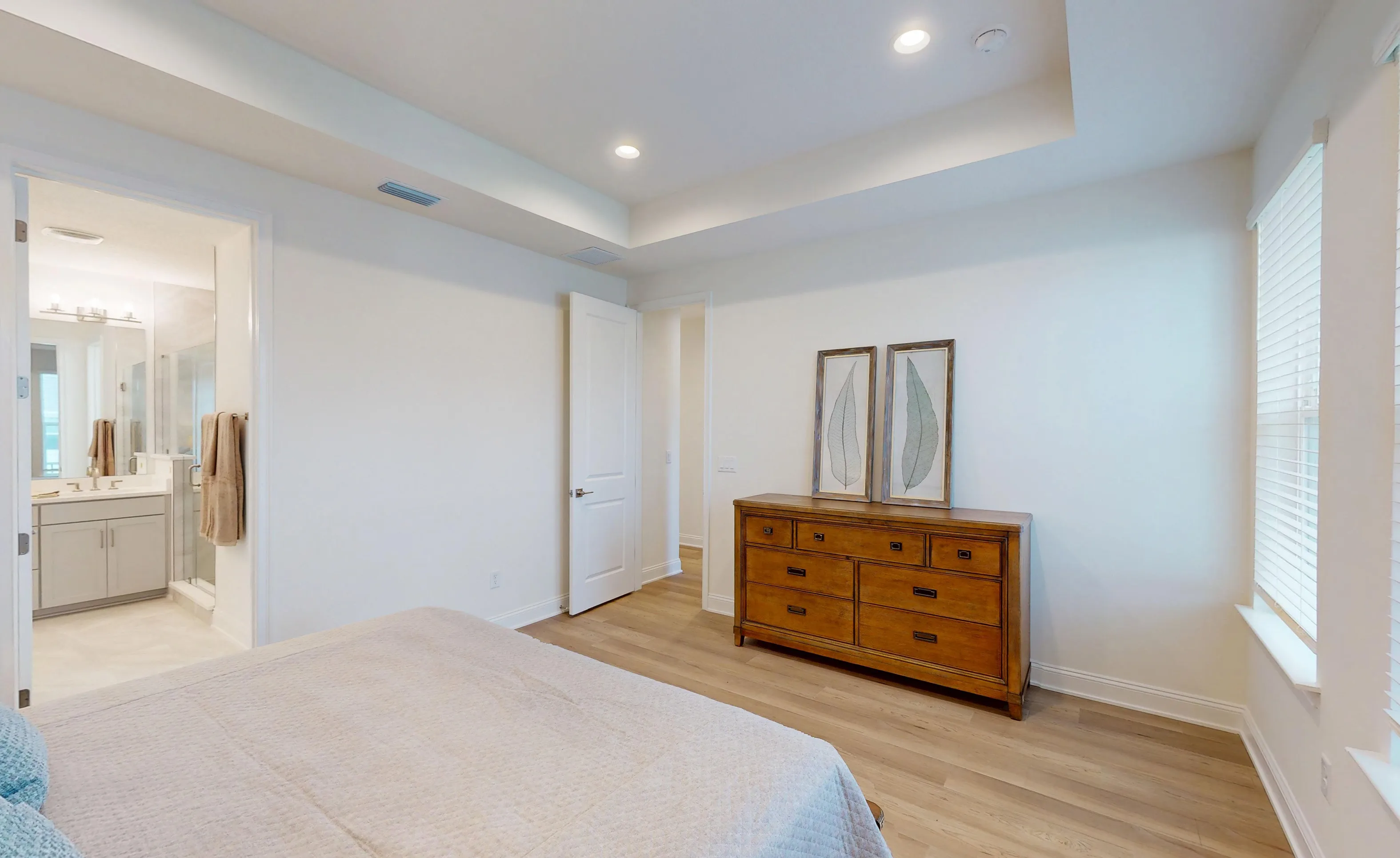 Primary bedroom with tray ceiling, wood-look flooring, a wood dresser, and an entrance to the en-suite bathroom.